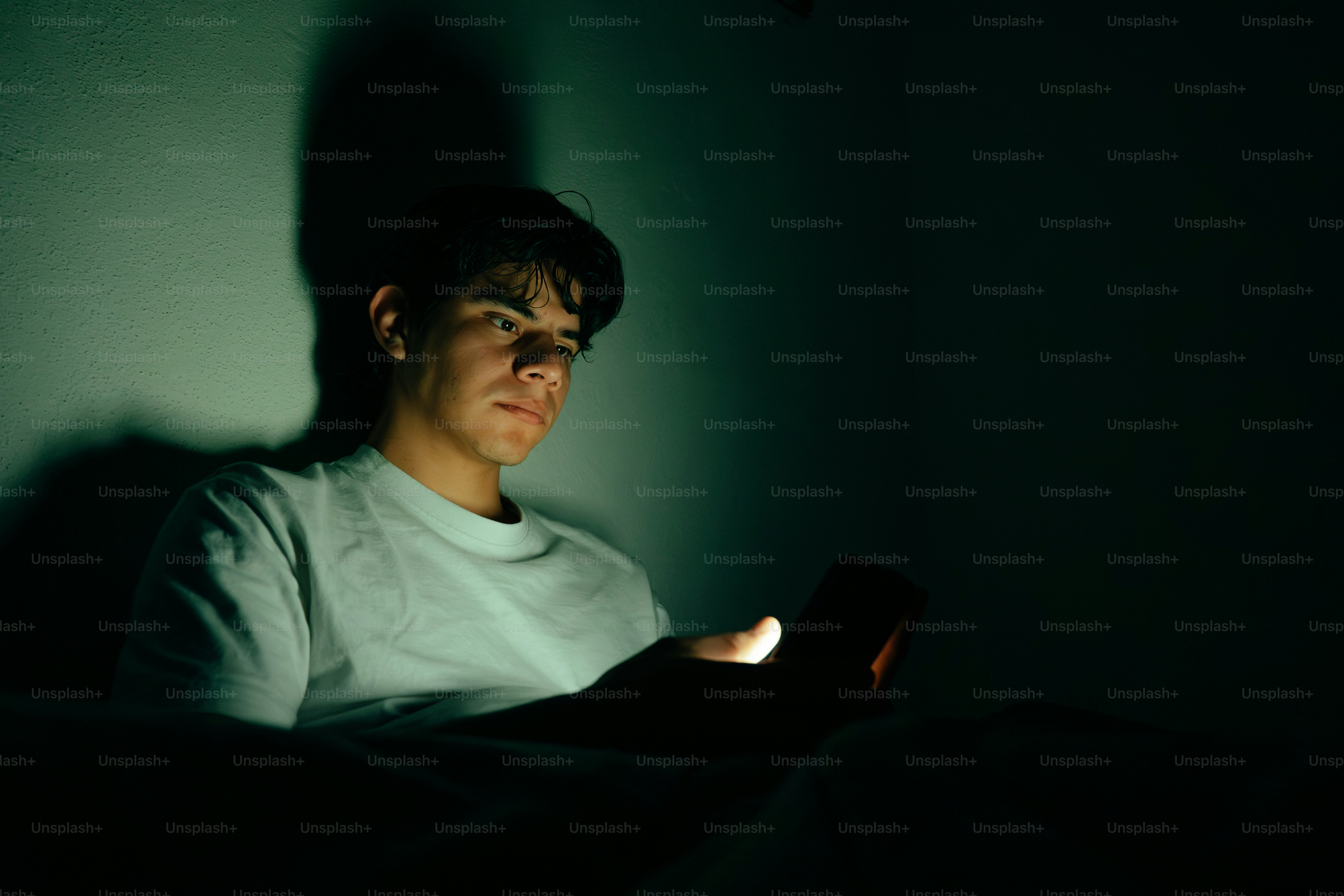 Young man illuminated by phone screen in dark room photo – Shadow Image ...