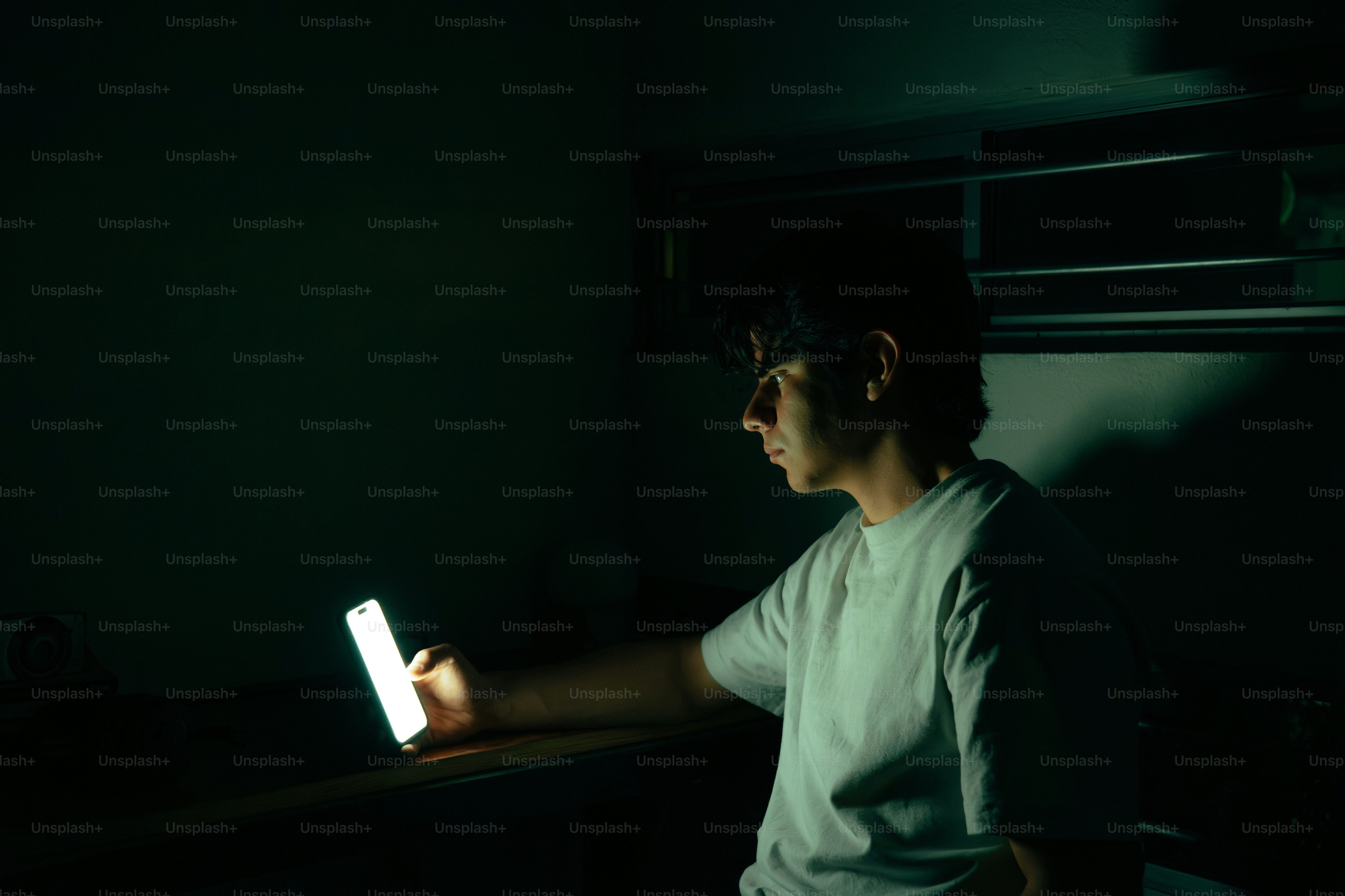 Young man illuminated by his phone screen at night.