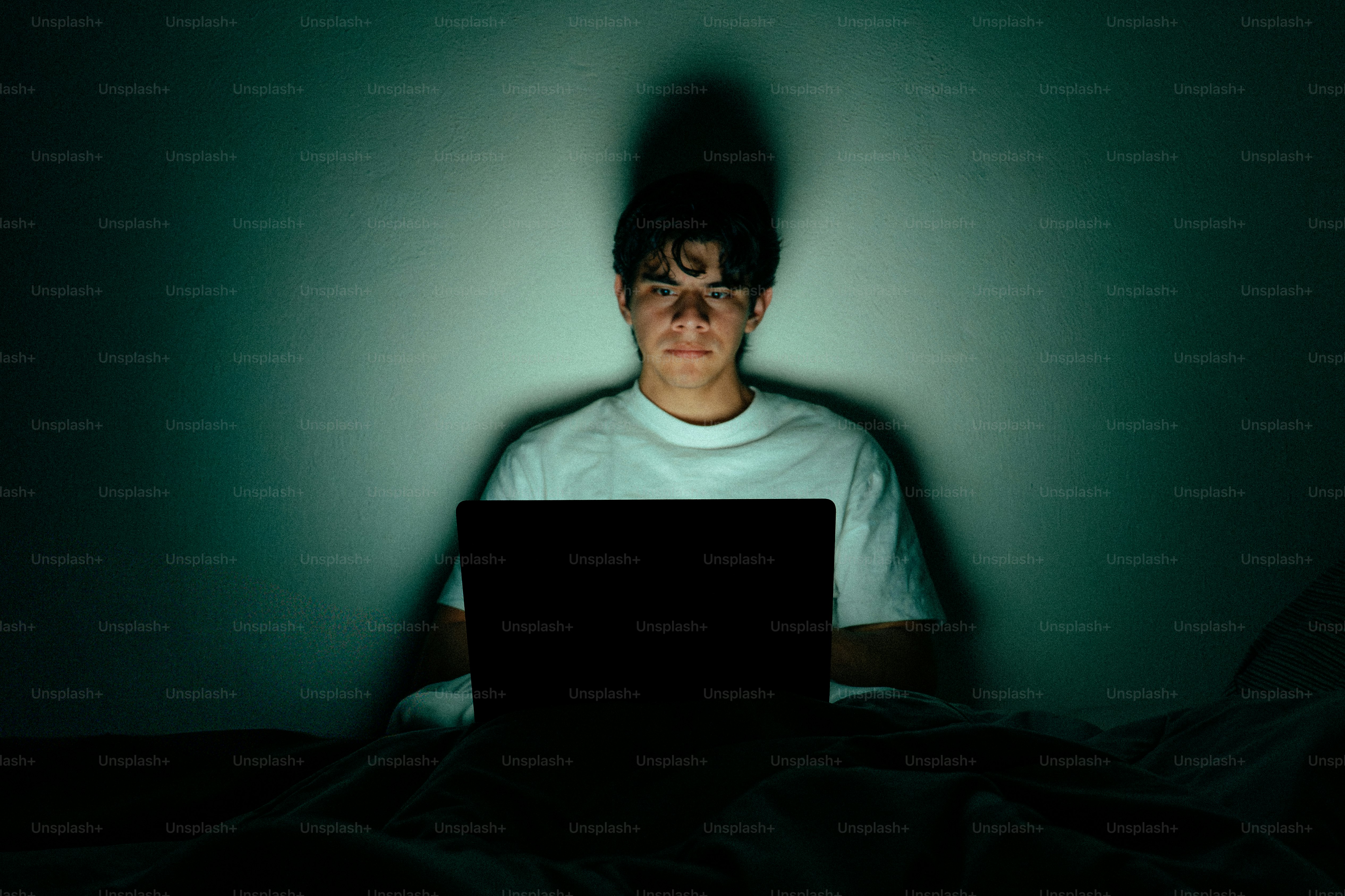 Teenager illuminated by laptop screen in dark room