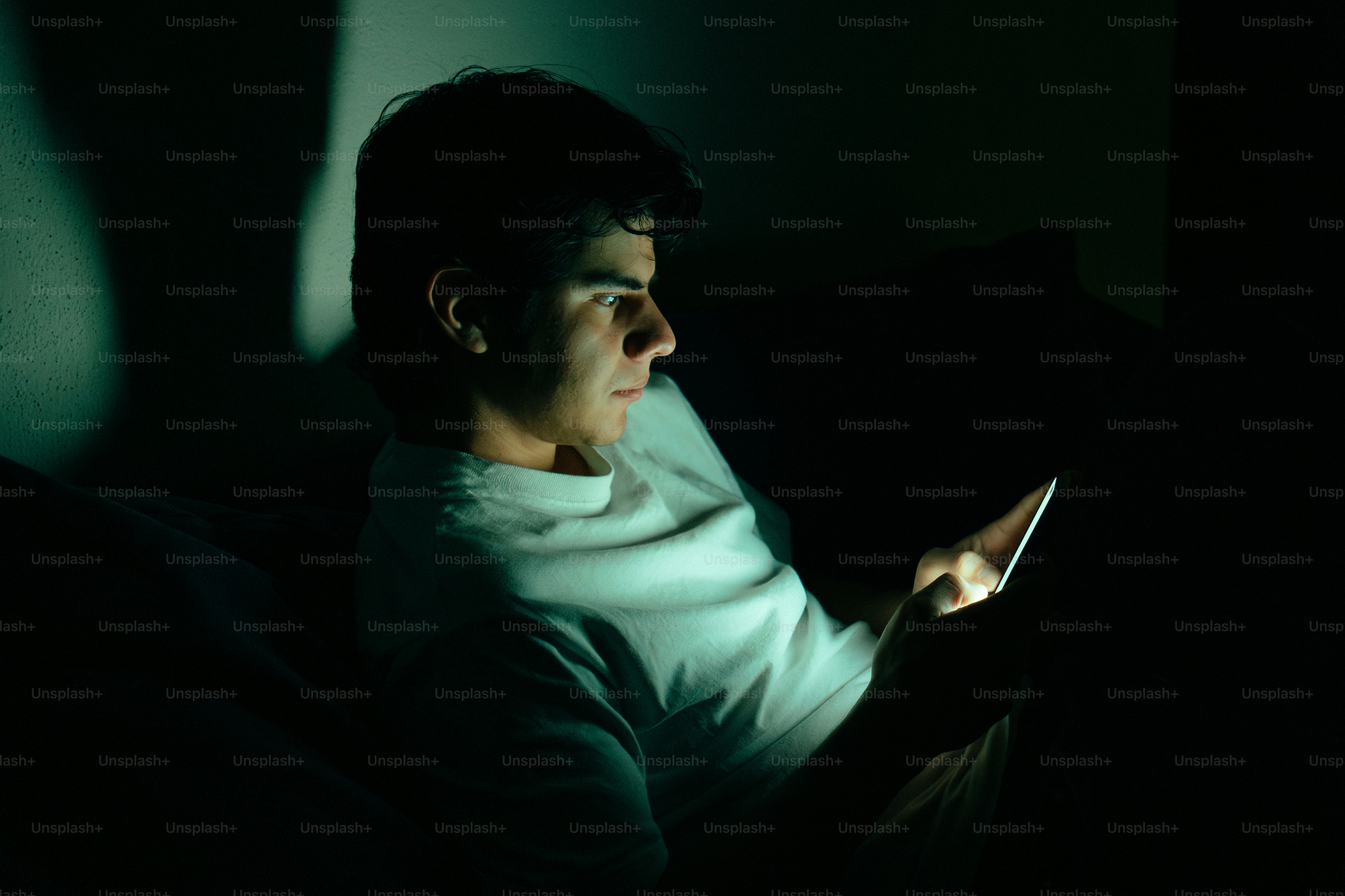 Young man illuminated by phone screen in dark room photo – Technology ...