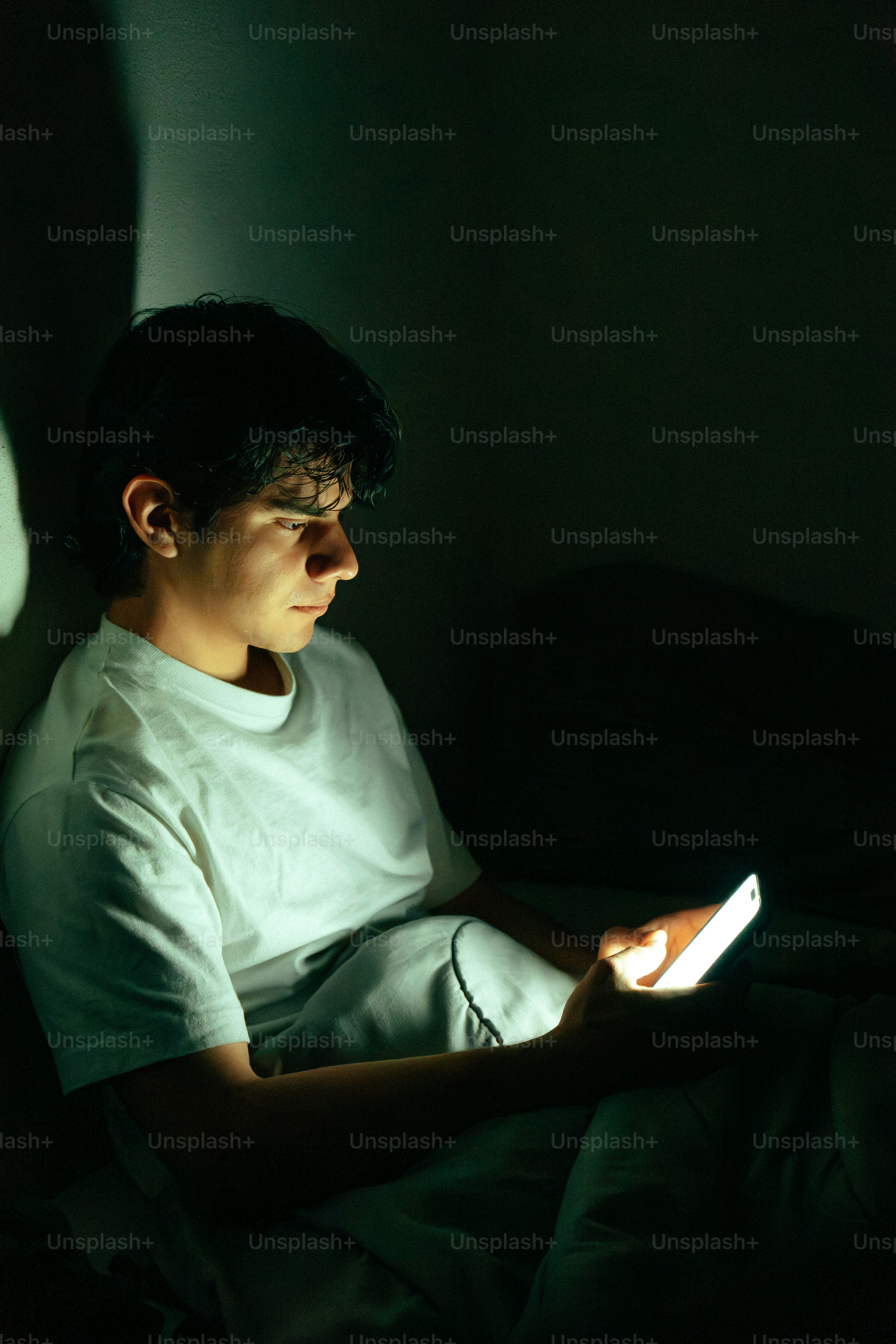 Young man illuminated by phone screen in dark room photo – Technology ...