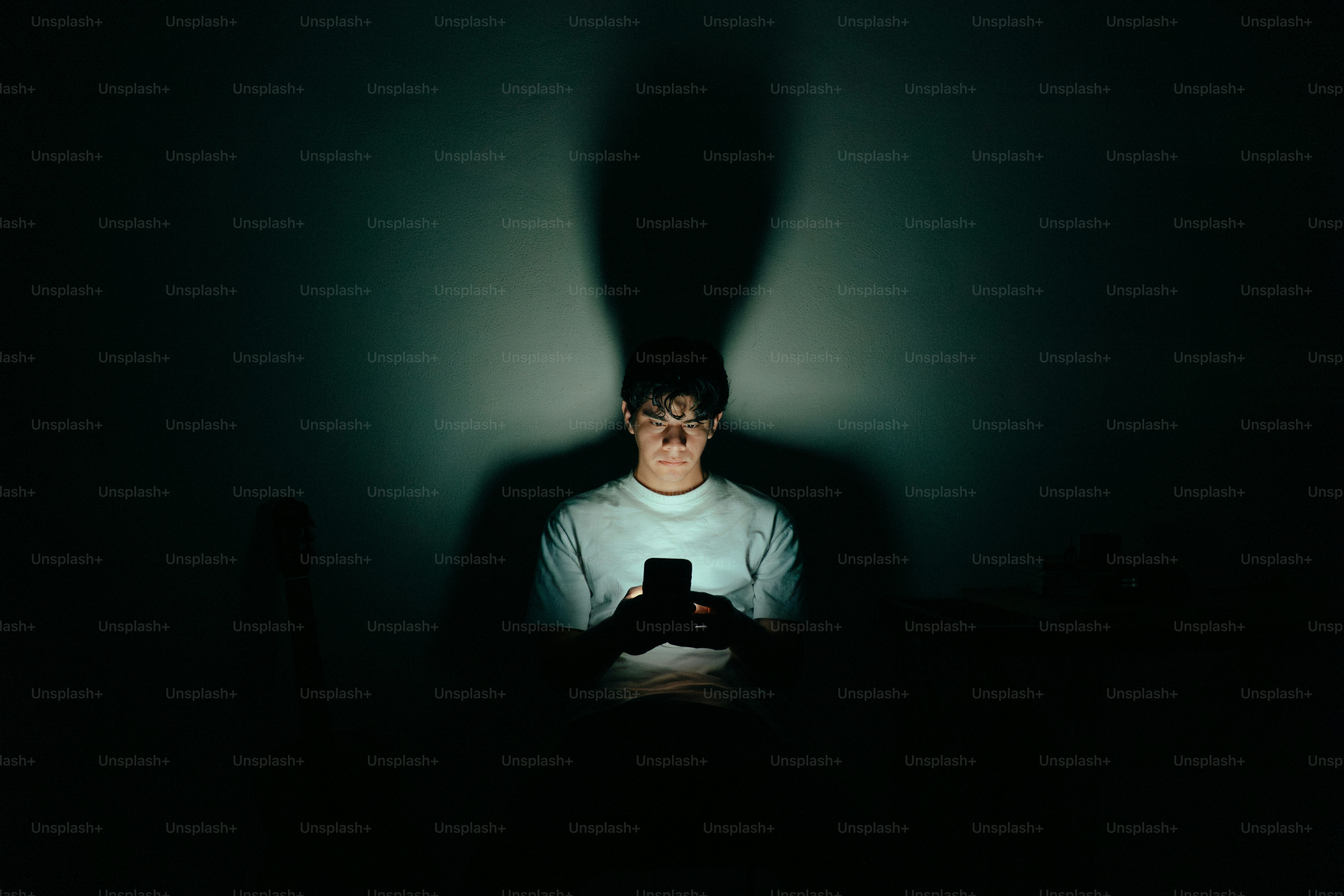Young man illuminated by phone screen in dark room photo – Technology ...