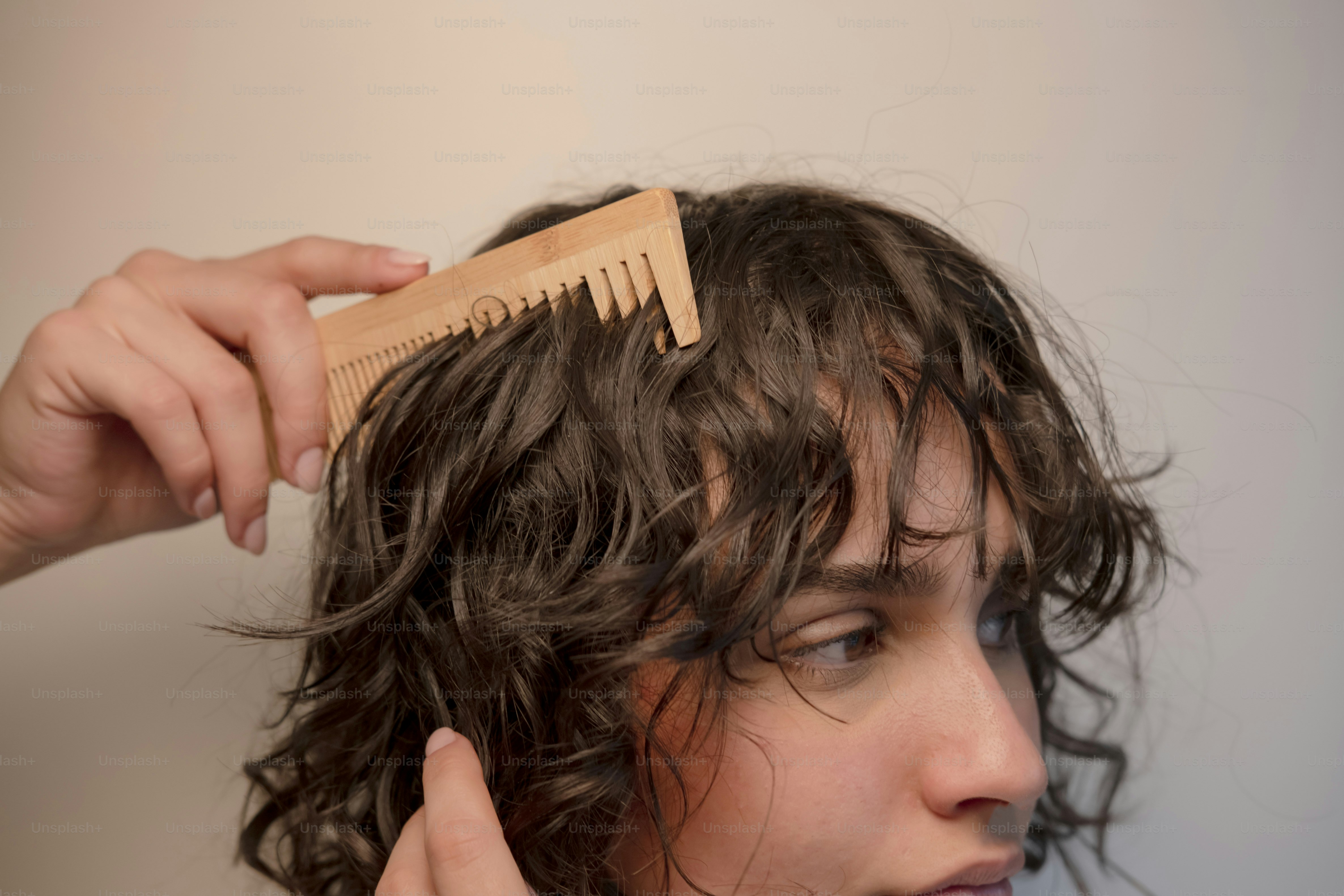 A hand combs curly brown hair with a wooden comb photo – Beauty Image ...