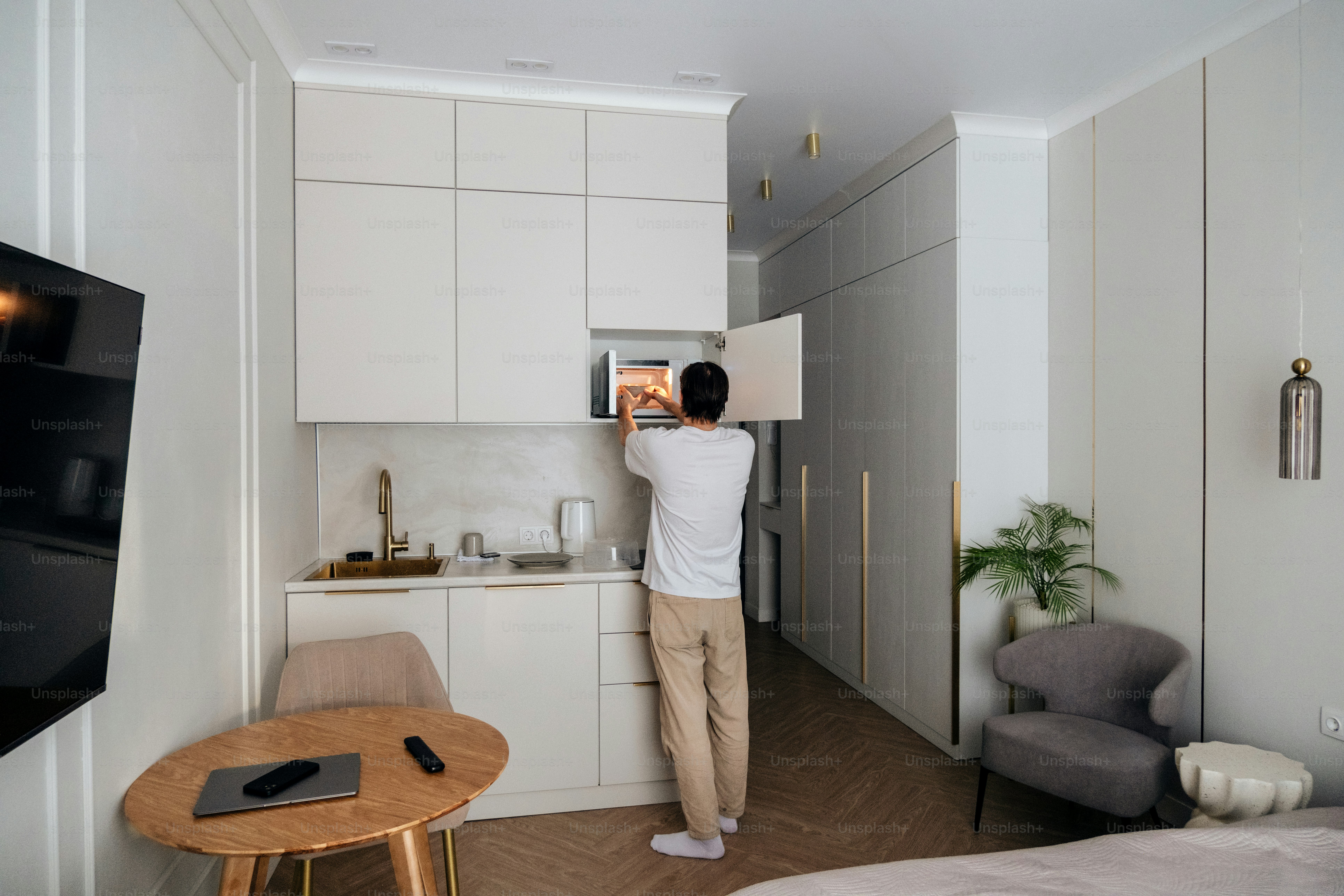 Man opening microwave in a modern studio apartment kitchen.