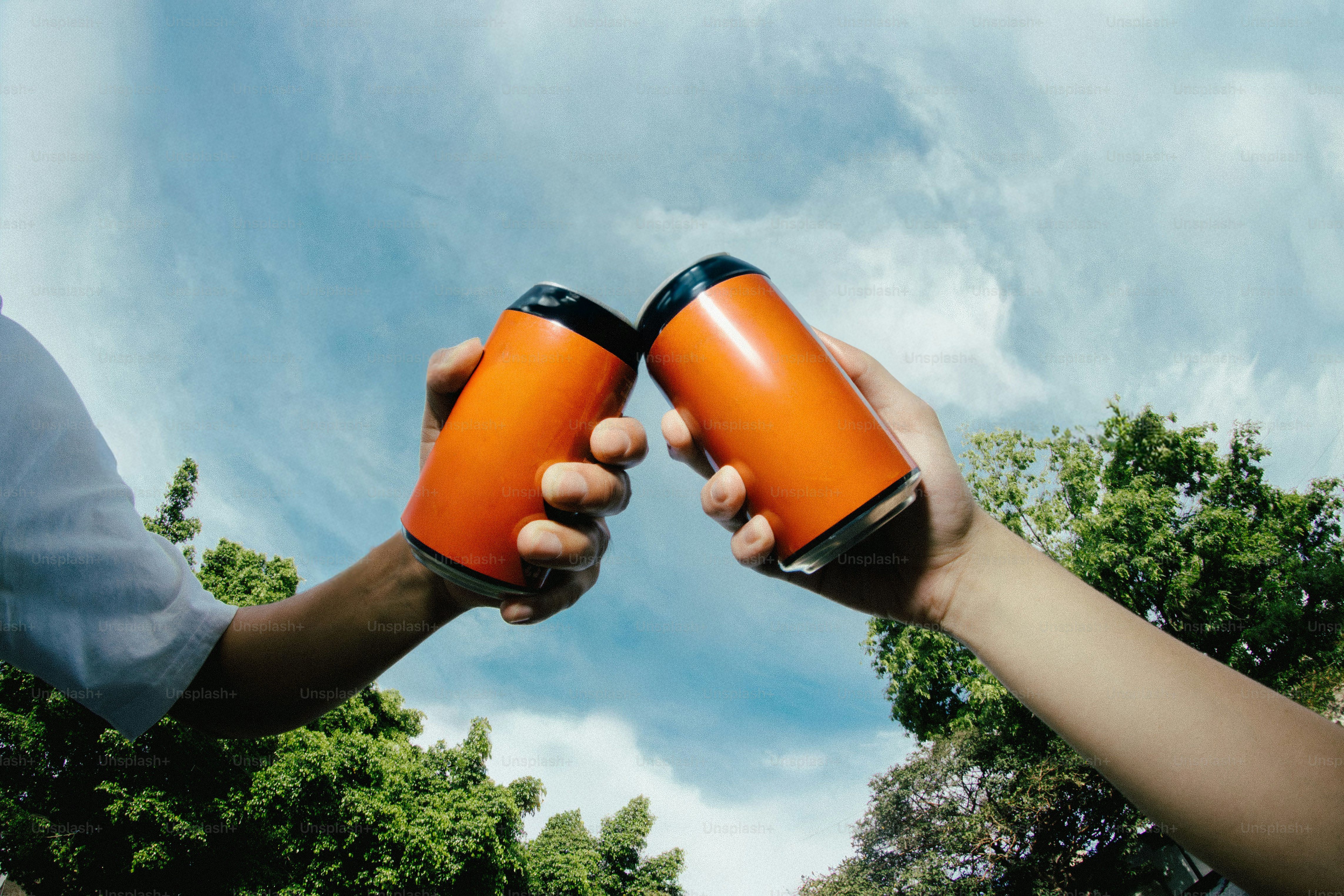 Due mani che tengono in alto lattine d'arancia in un toast