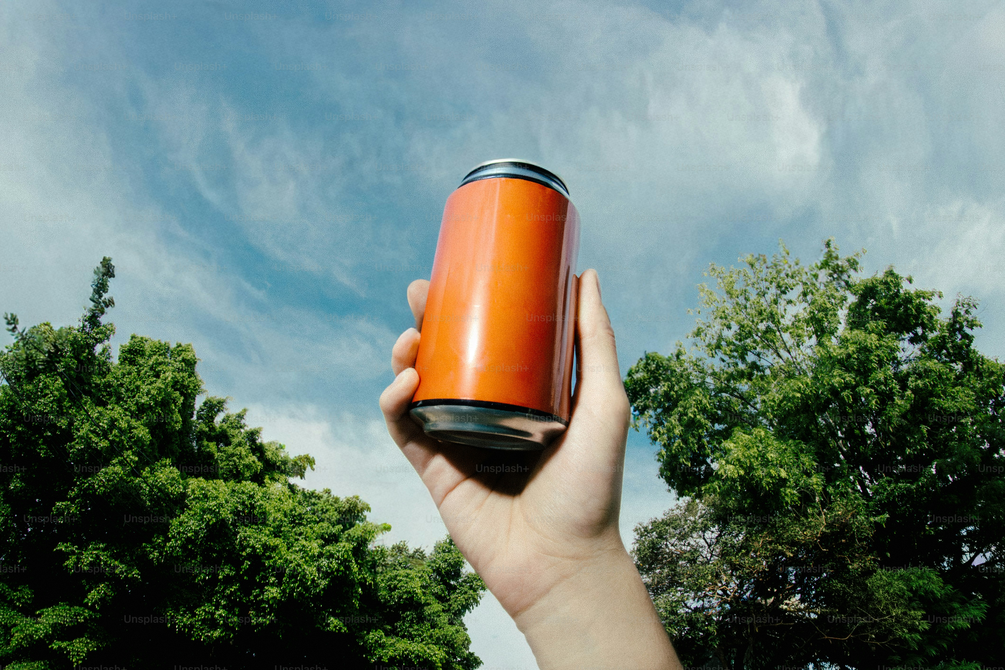 Mano che tiene una lattina arancione contro un cielo azzurro.