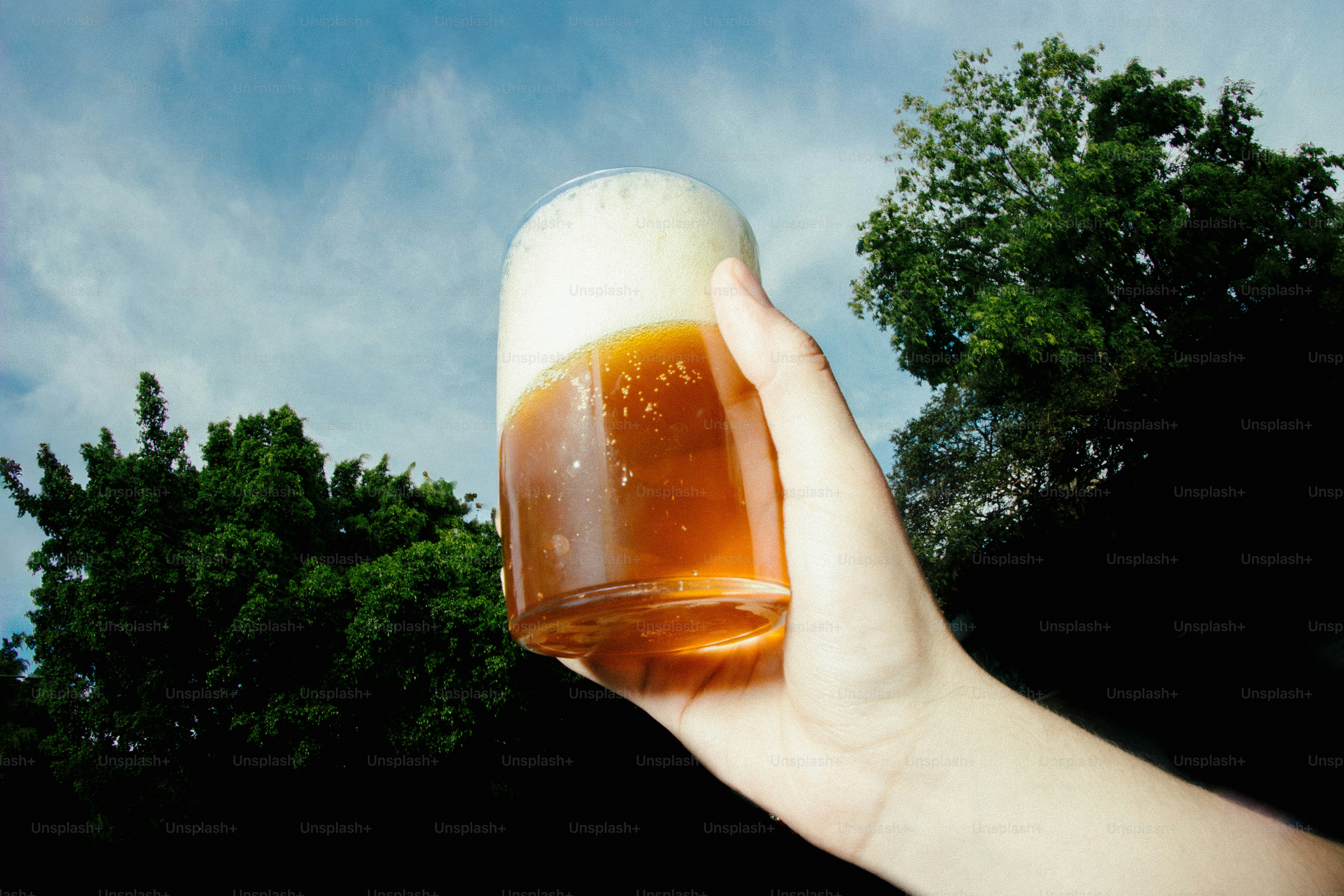 Mano che tiene una birra schiumosa contro un cielo nuvoloso.