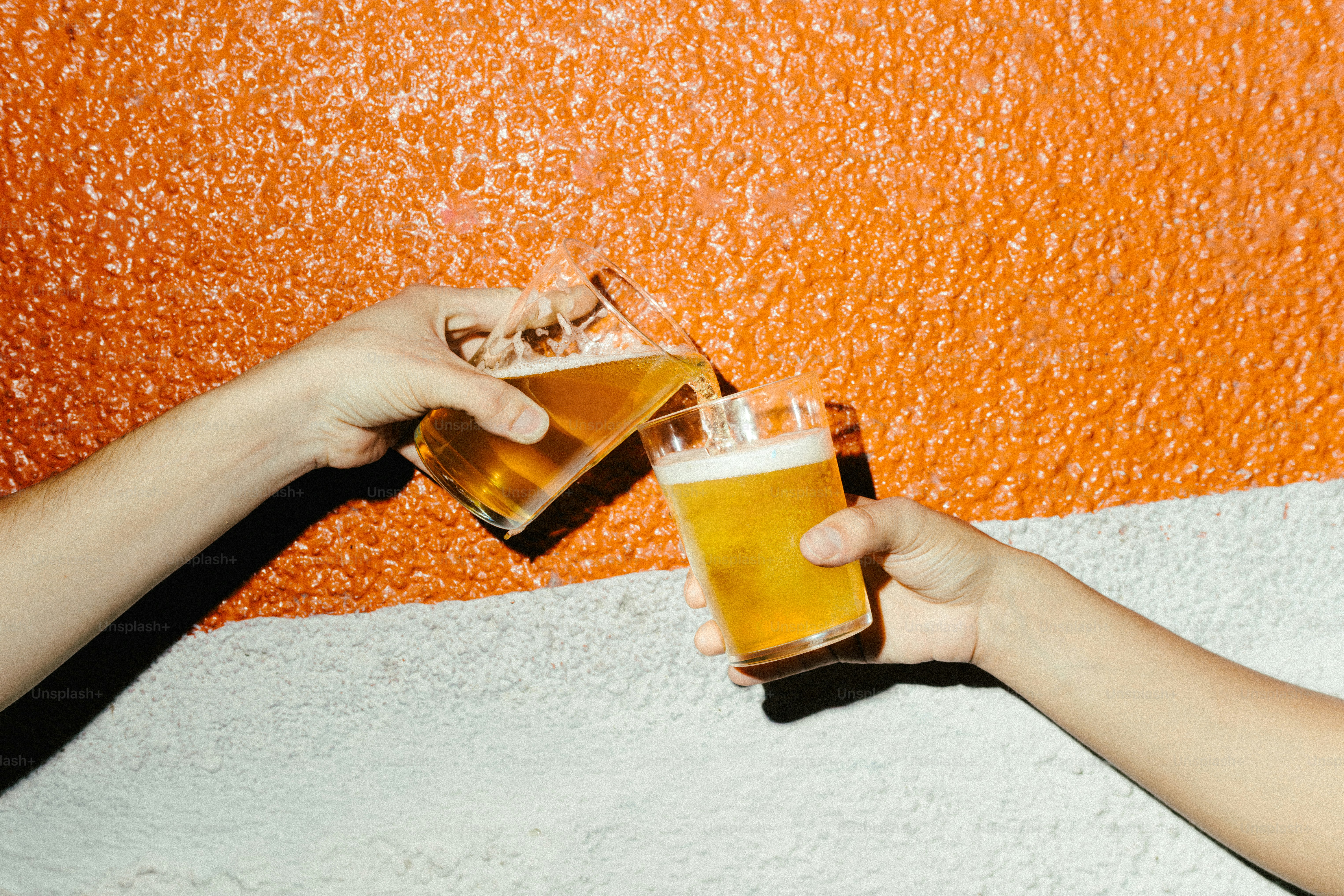 Due mani che tintinnano bicchieri di birra contro la parete arancione