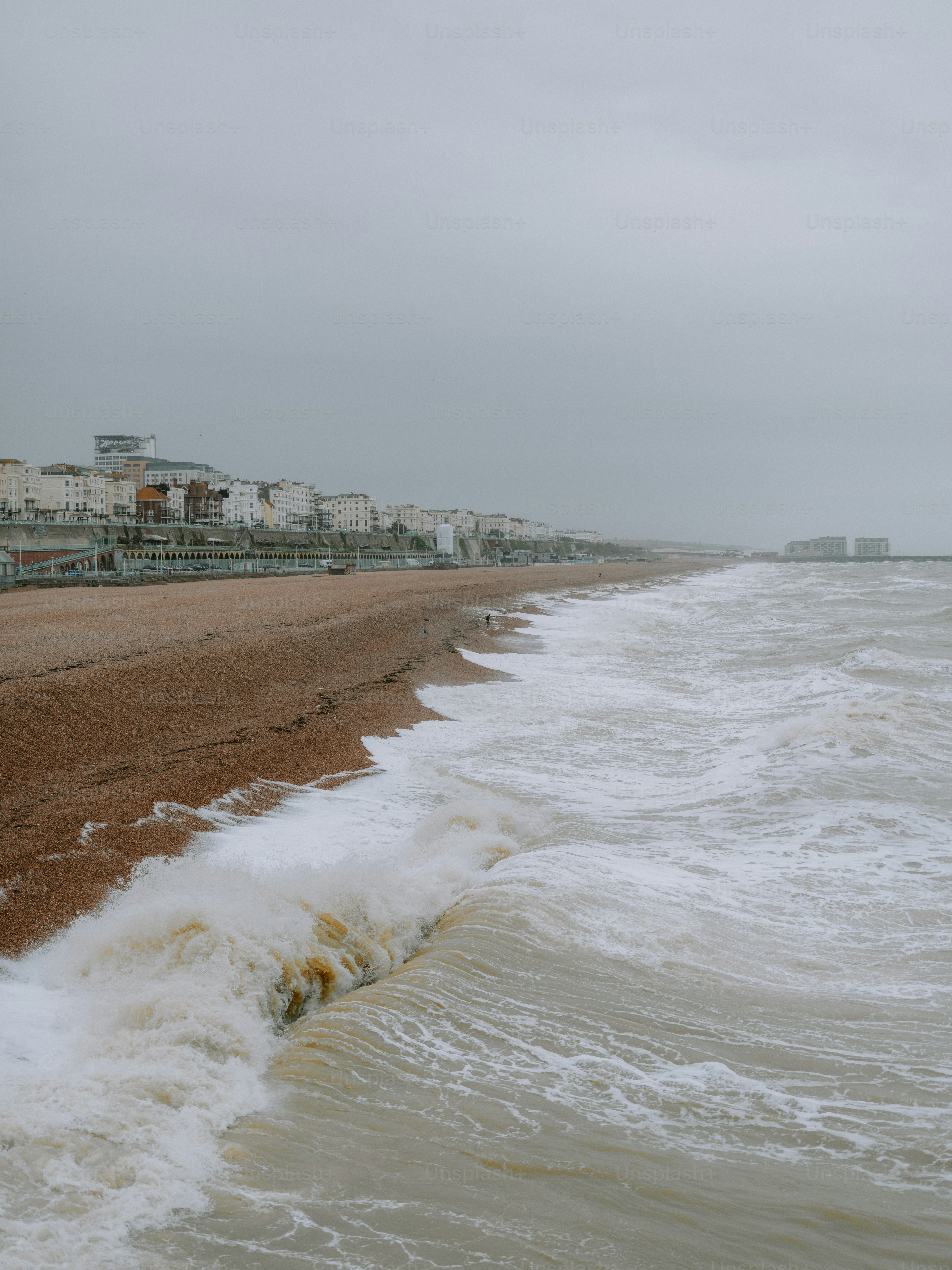 Waves crashing on a pebble beach with buildings in background