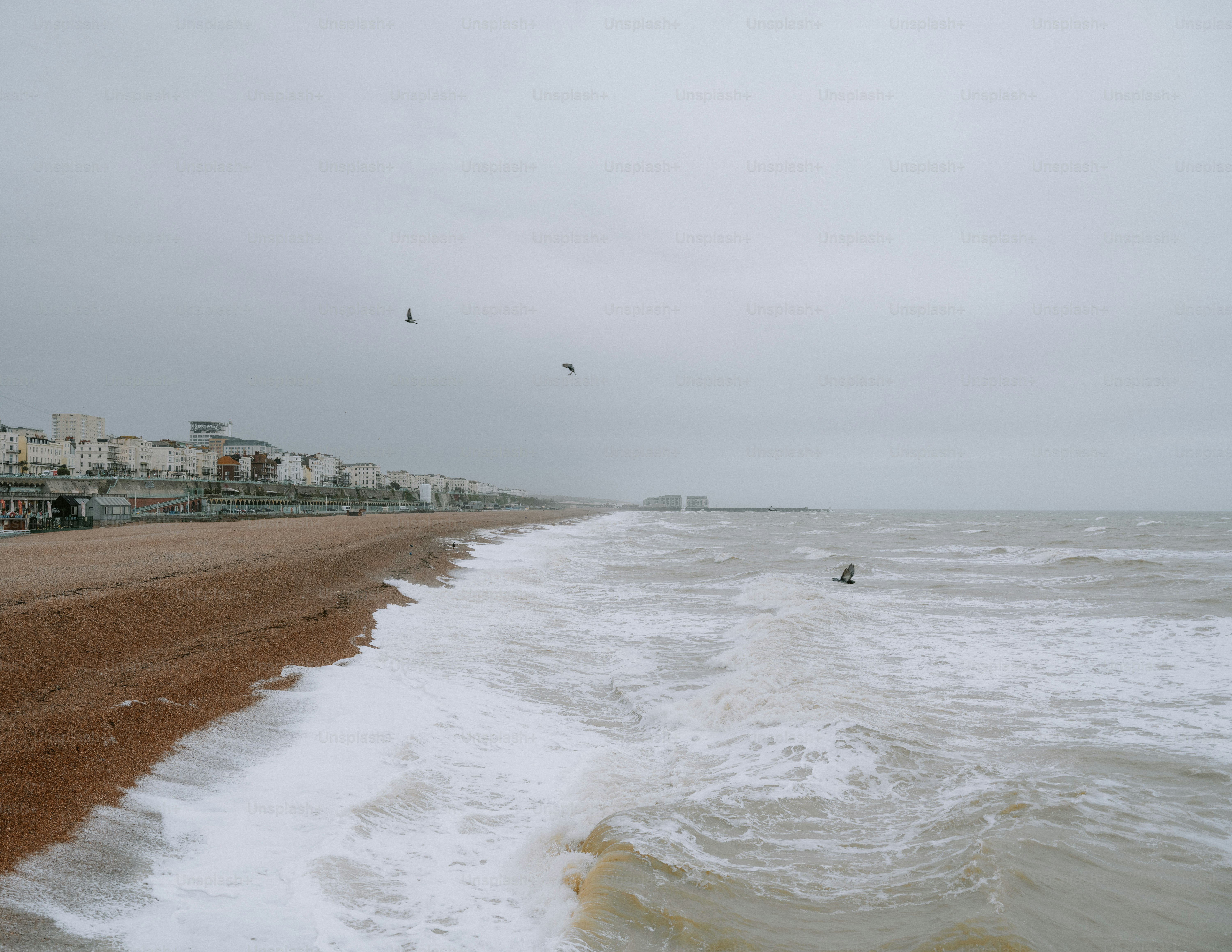 A beach with waves and buildings under a cloudy sky.