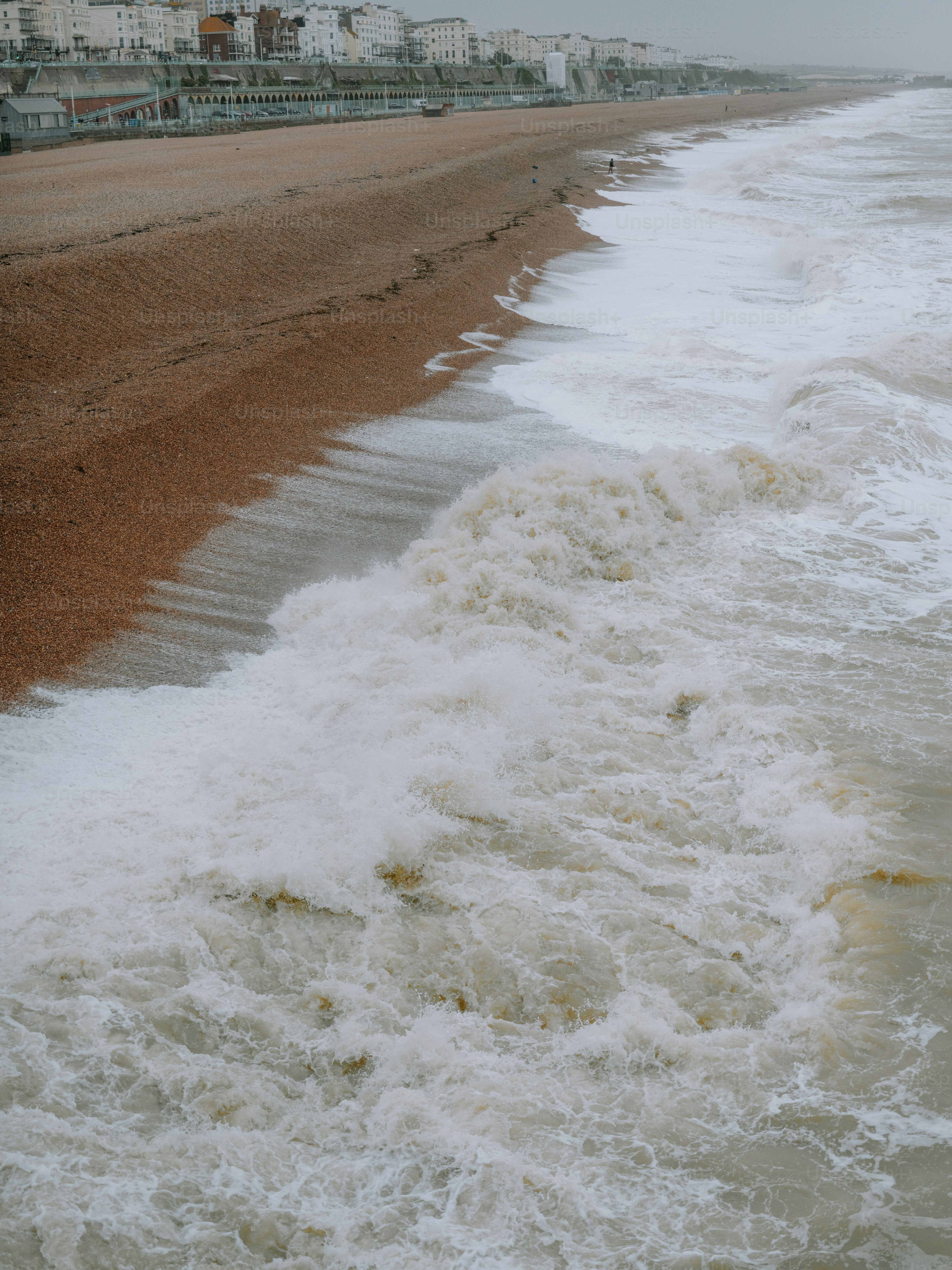 Waves crashing on a pebble beach with buildings in background