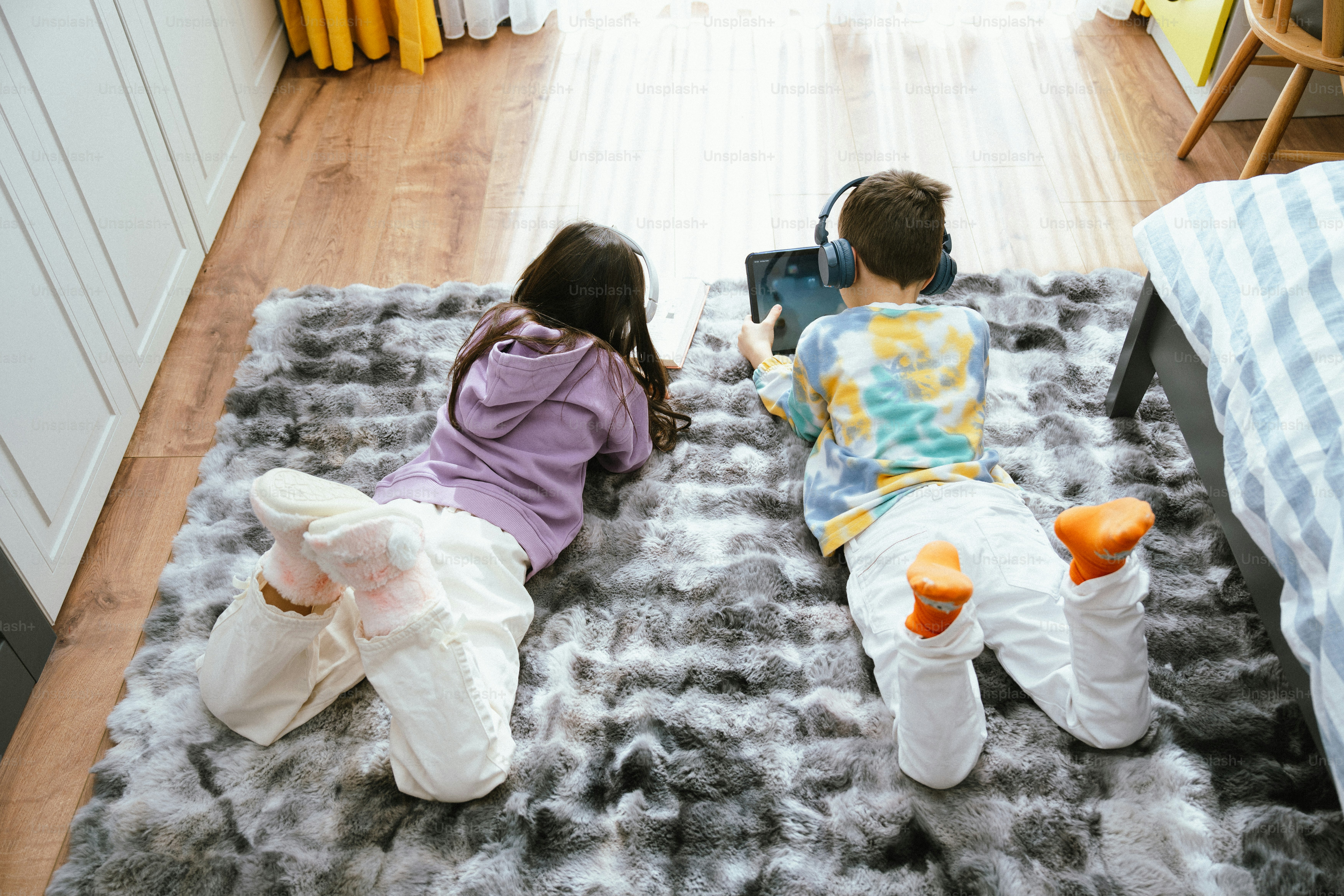 Dos niños yacen en una alfombra usando una tableta