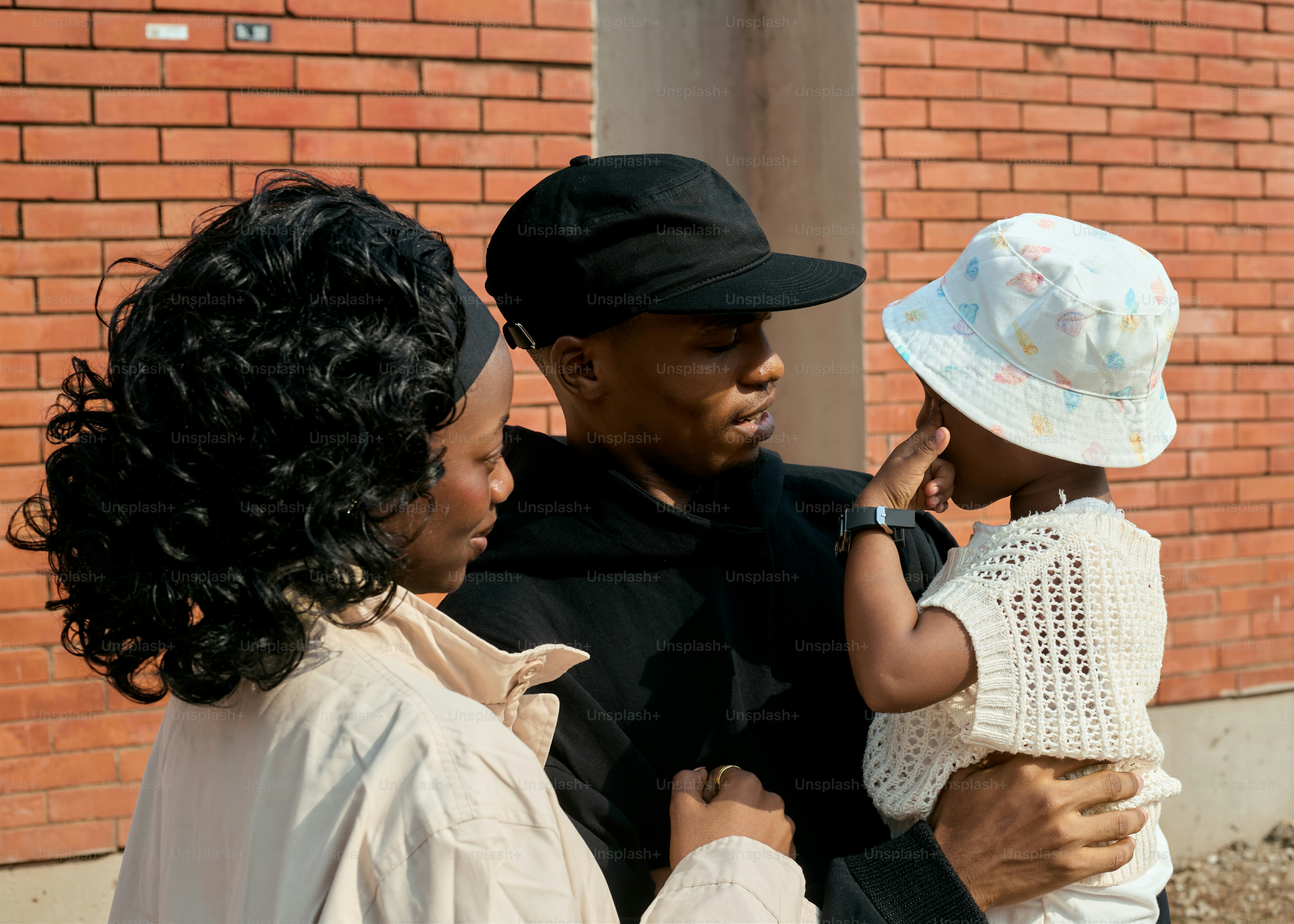 Parents holding their young child in front of brick wall photo – Family ...