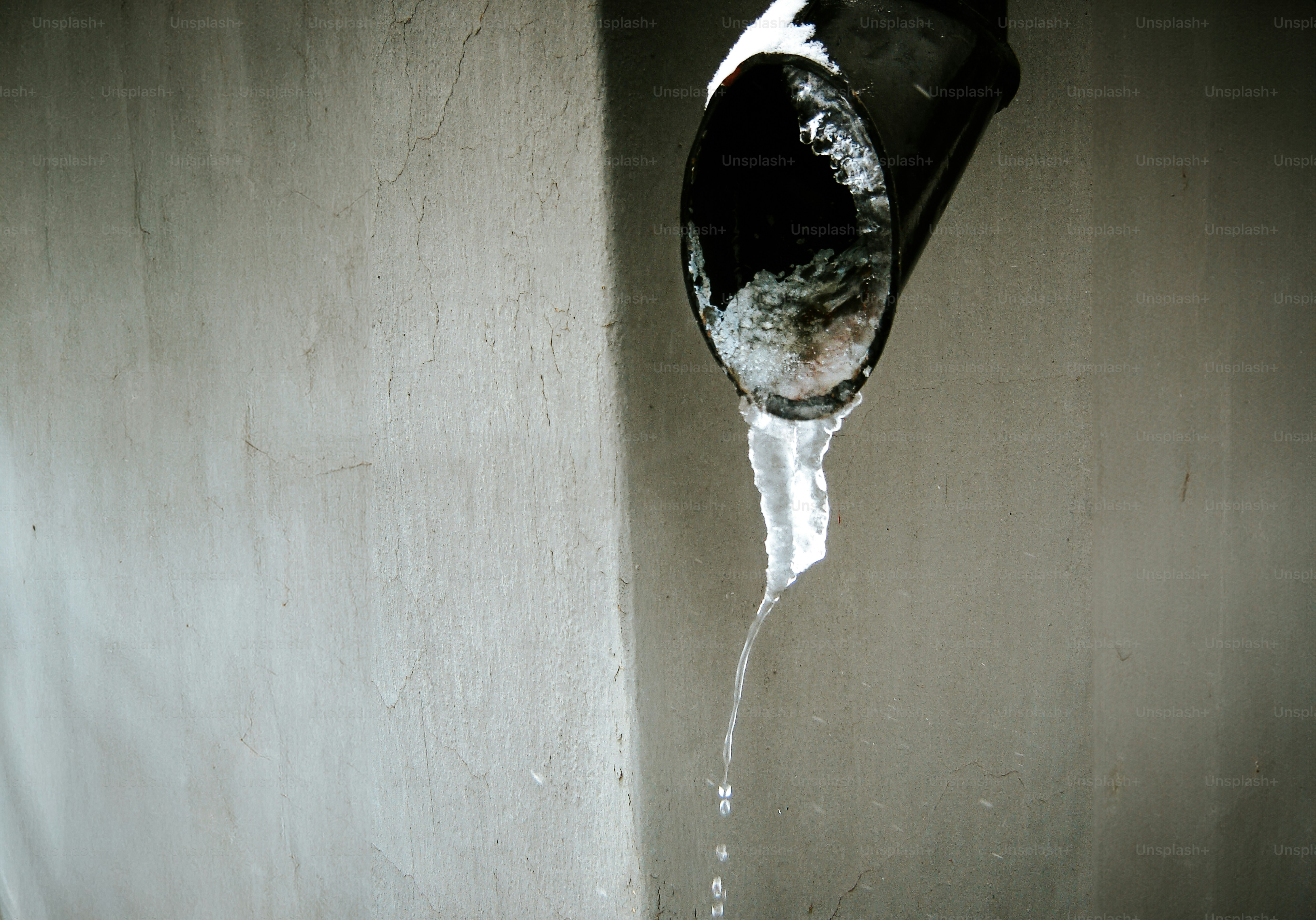 Water dripping from a dark pipe onto a textured wall.
