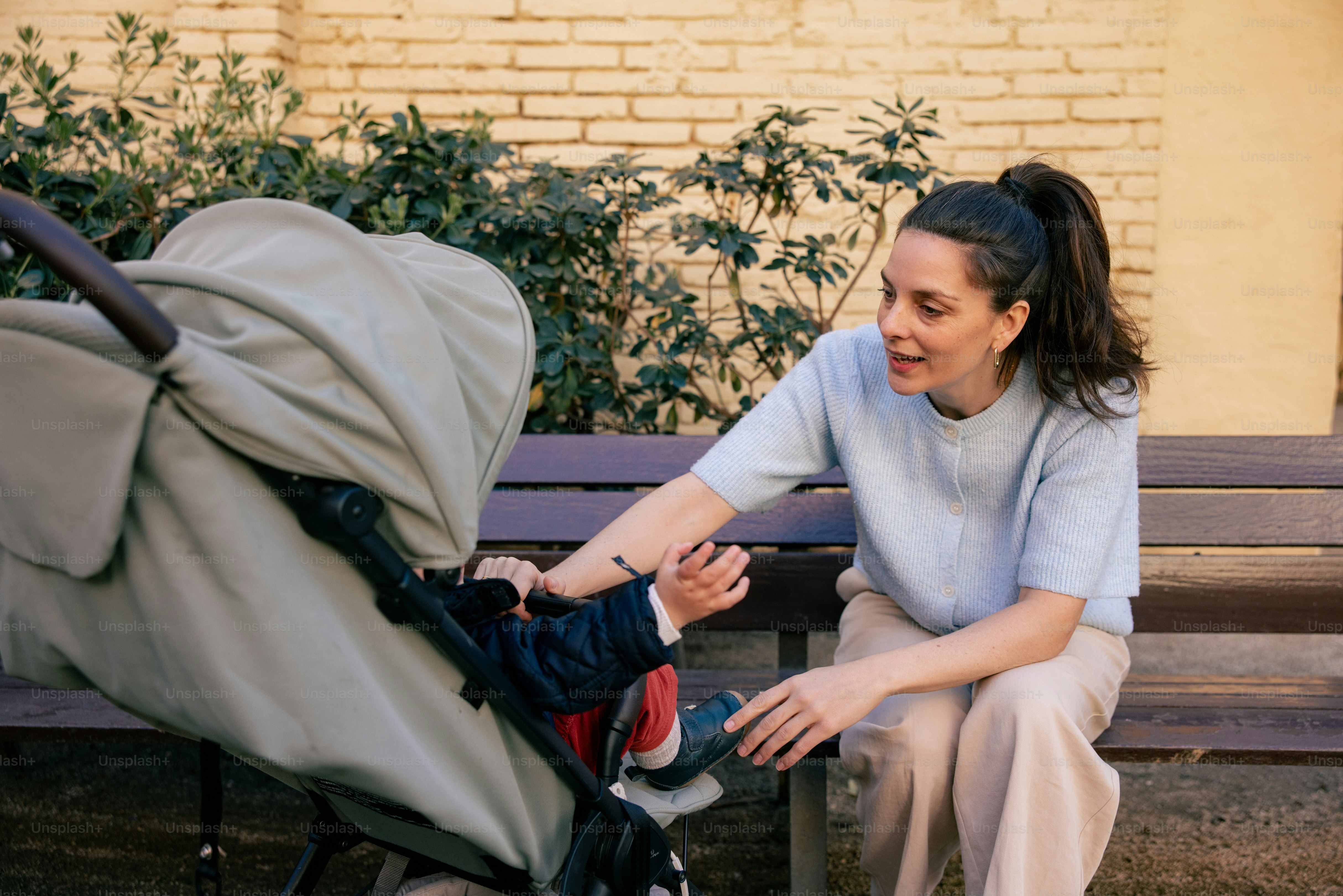 Mutter berührt den Fuß des Babys im Kinderwagen auf der Bank