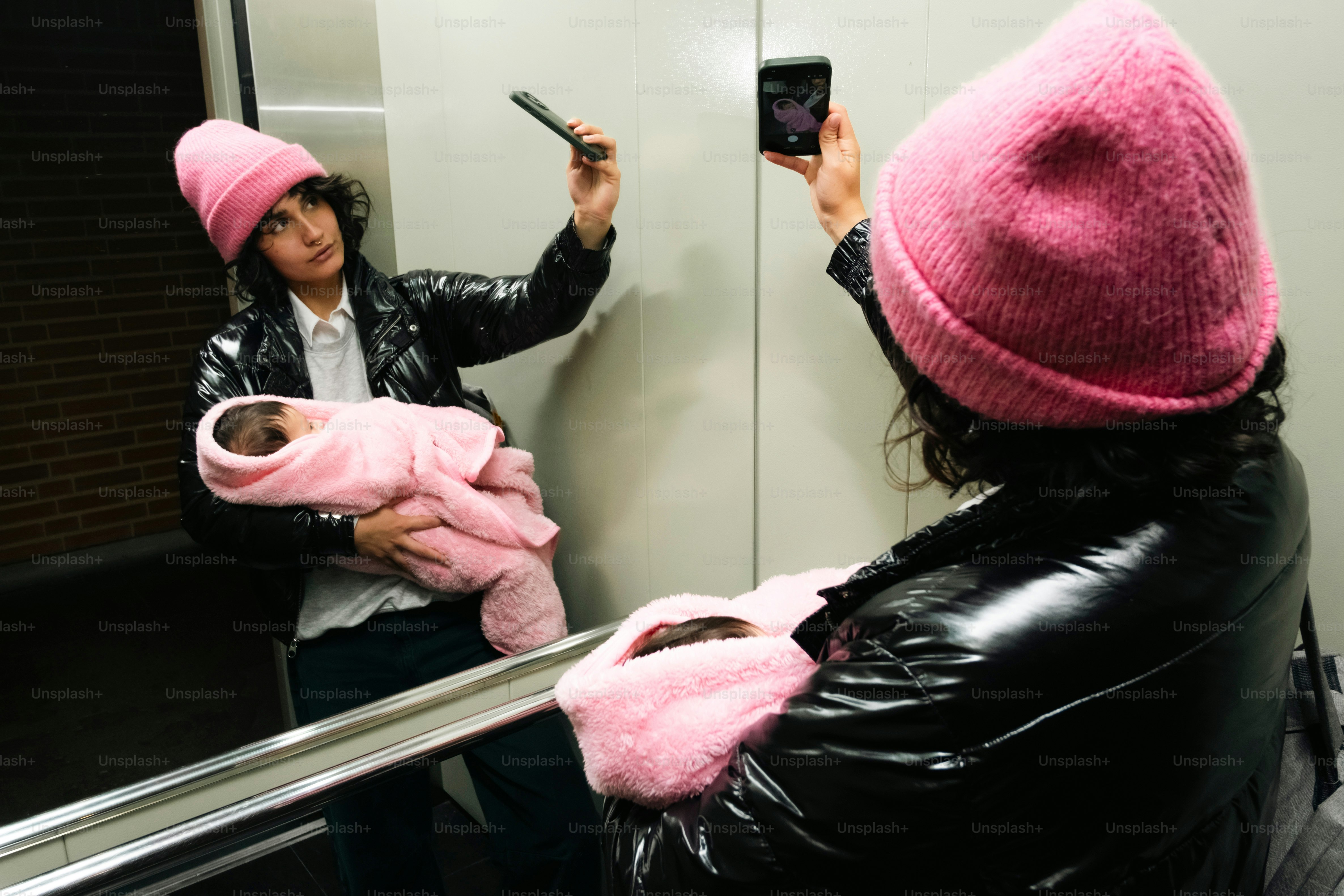 Wanita bertopi merah muda menggendong bayi, mengambil selfie.