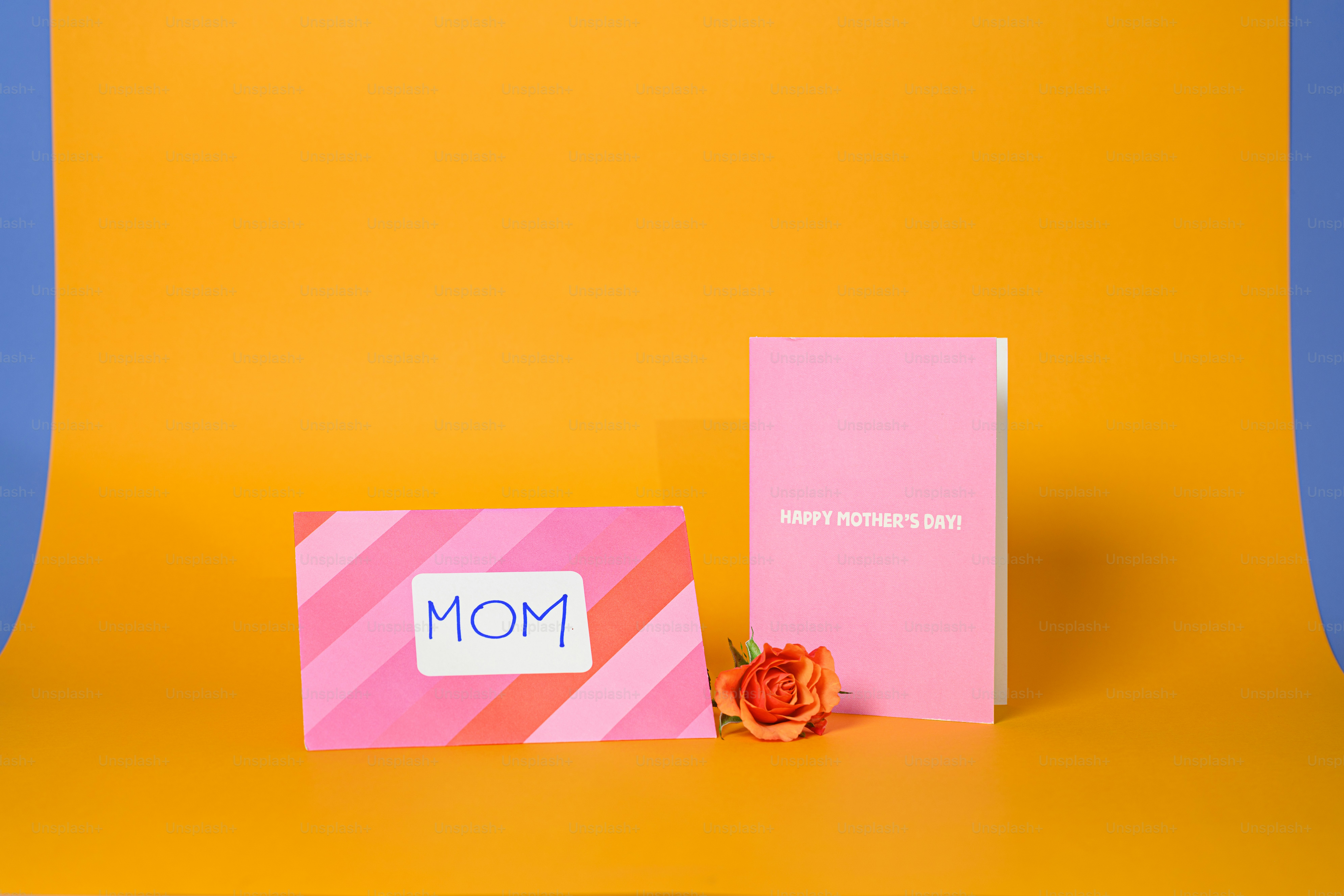 Dos tarjetas rosas y una rosa sobre fondo naranja