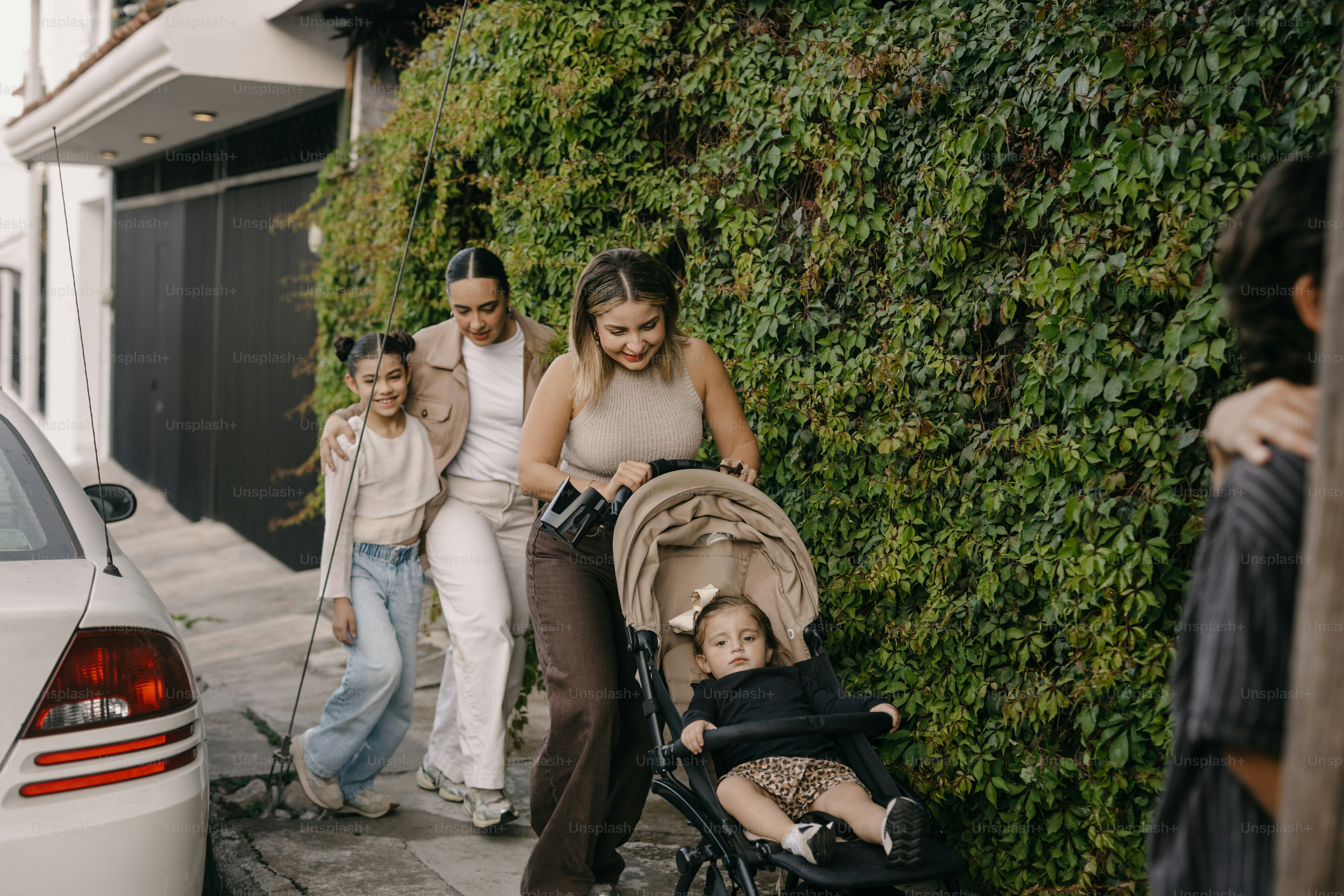 Des femmes et des enfants marchent sur un trottoir avec une poussette.