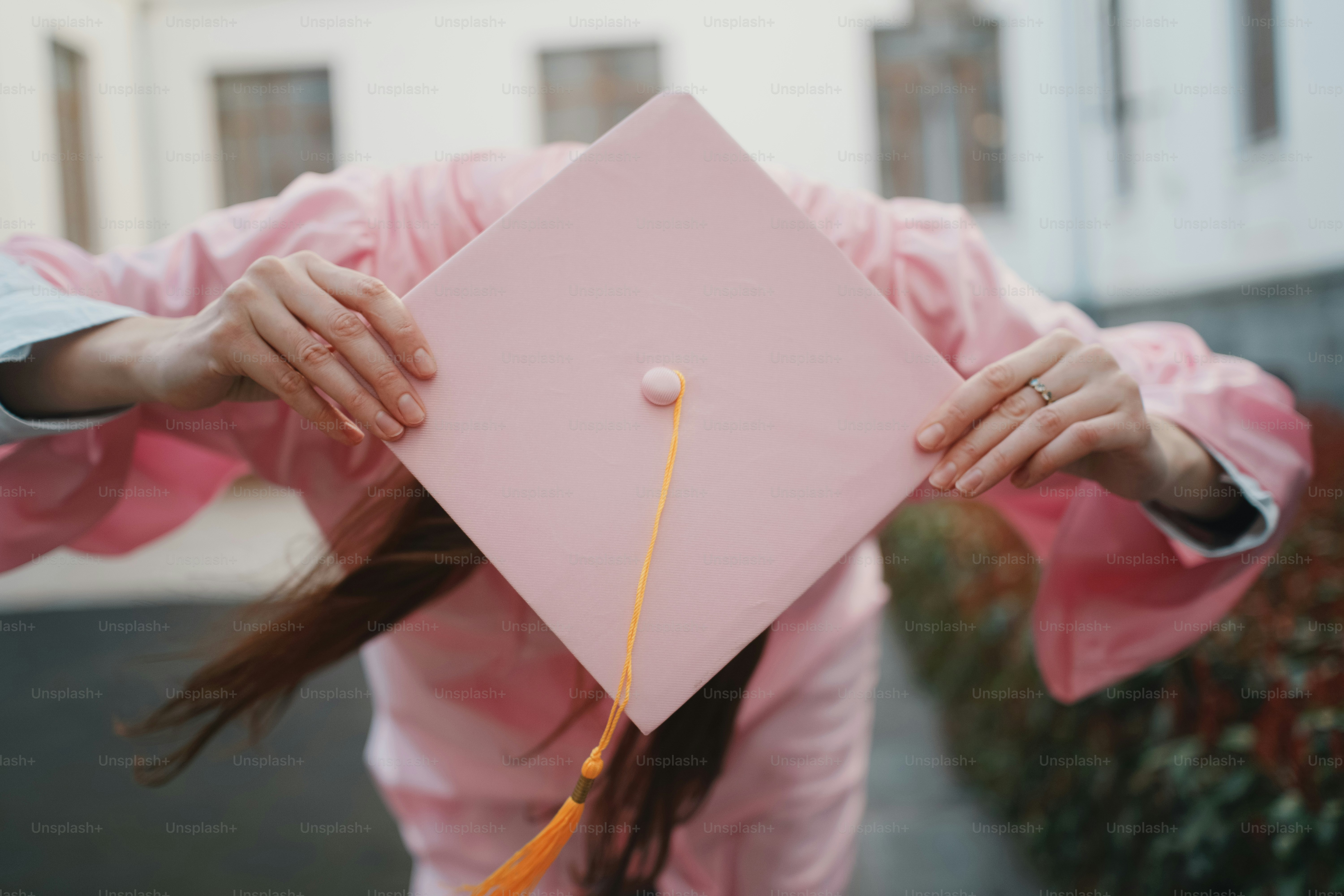 Person in graduation gown holding pink cap