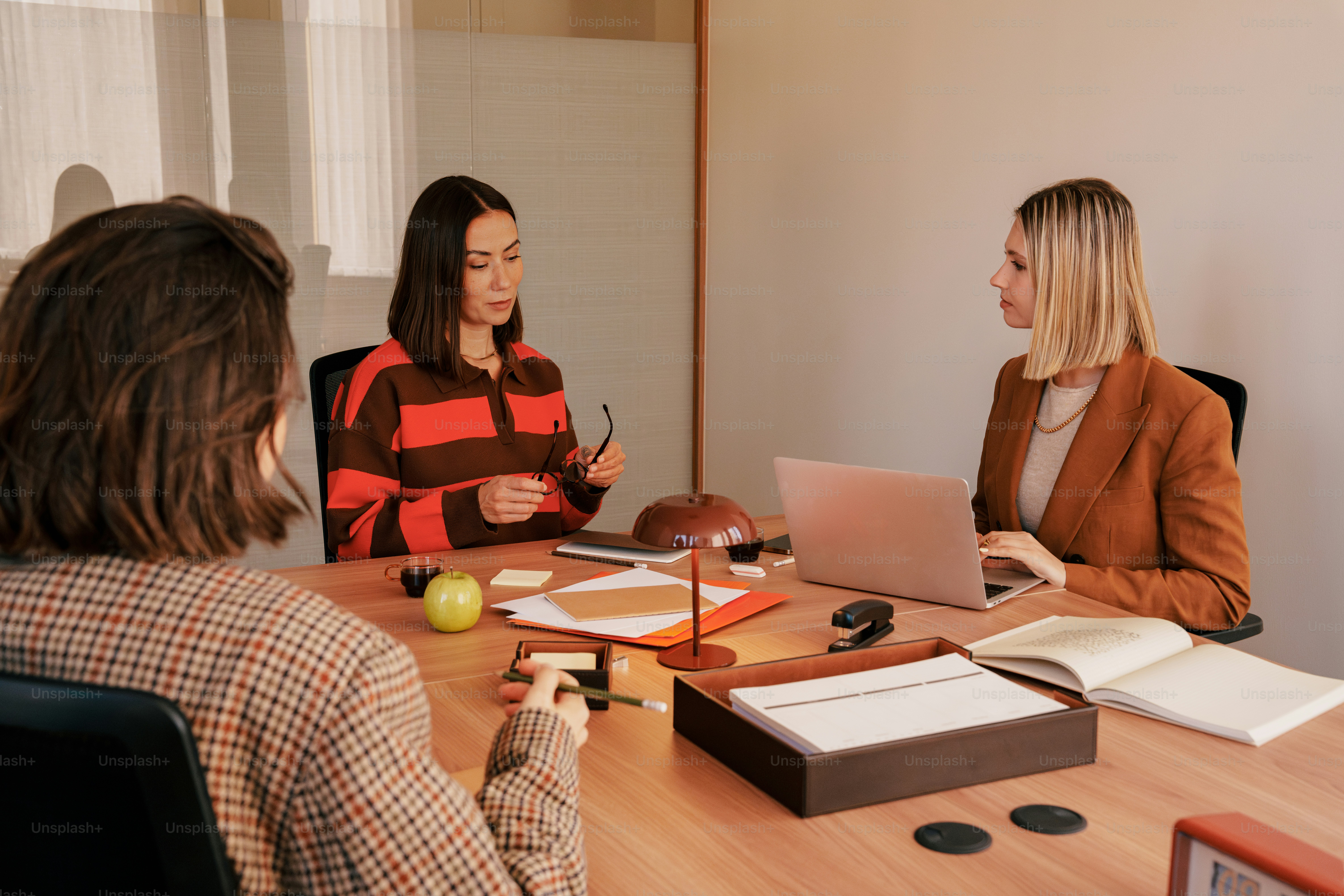 Tiga wanita dalam pertemuan bisnis di sekitar meja.