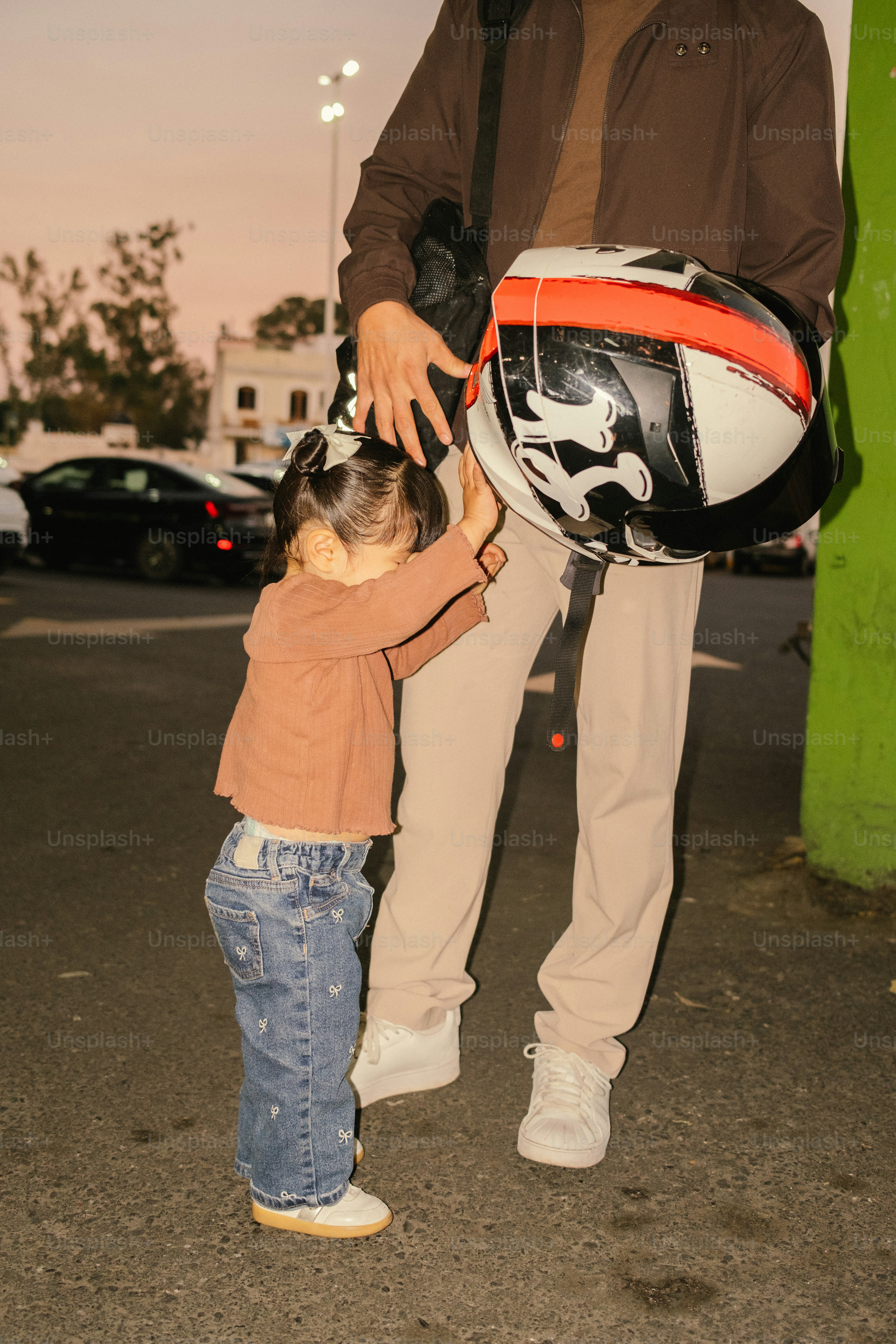Anak meraih helm yang dipegang oleh orang dewasa.