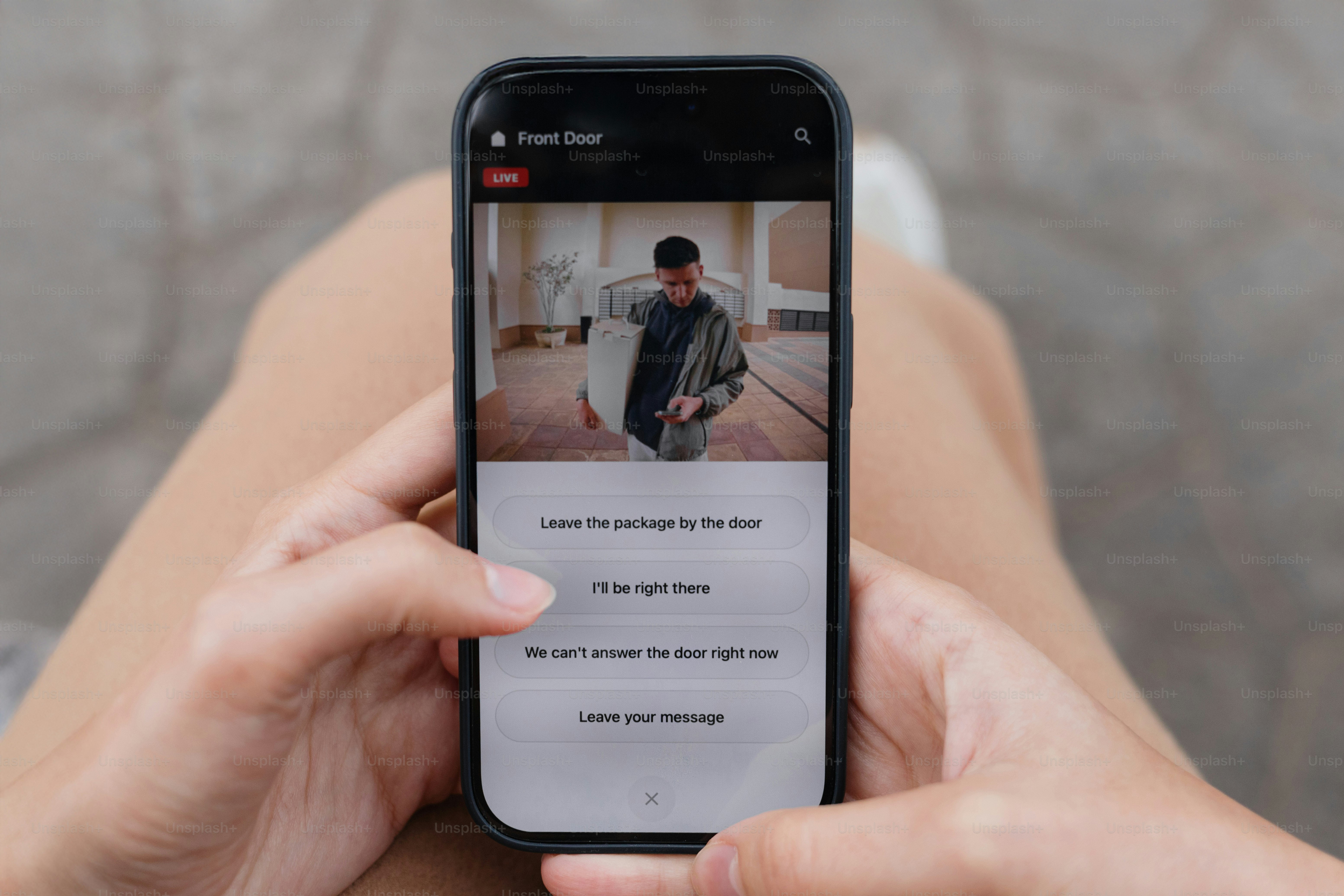 Person checking smart doorbell camera on smartphone, viewing delivery man at front door