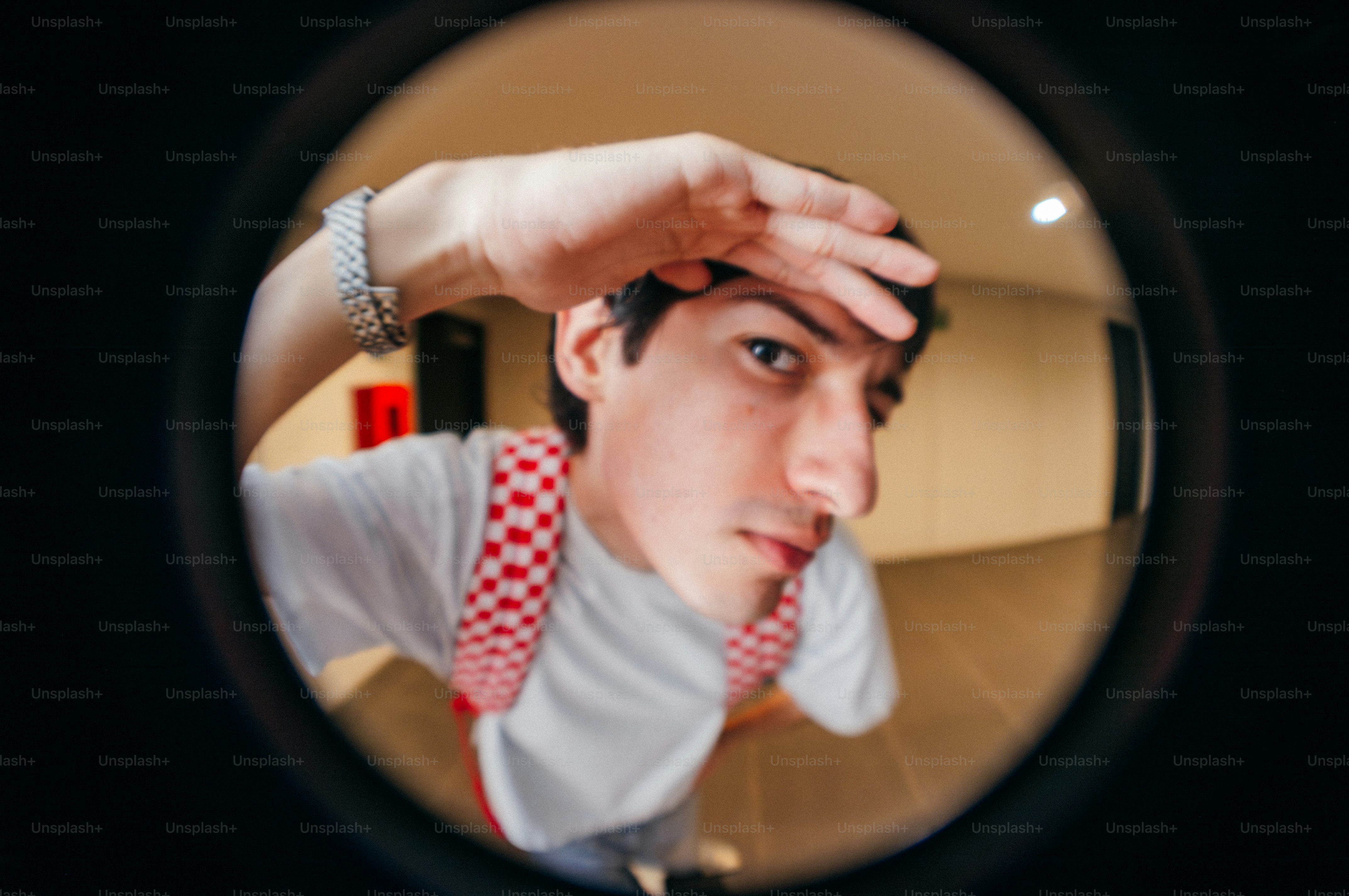 Young man peeking through a fisheye lens.