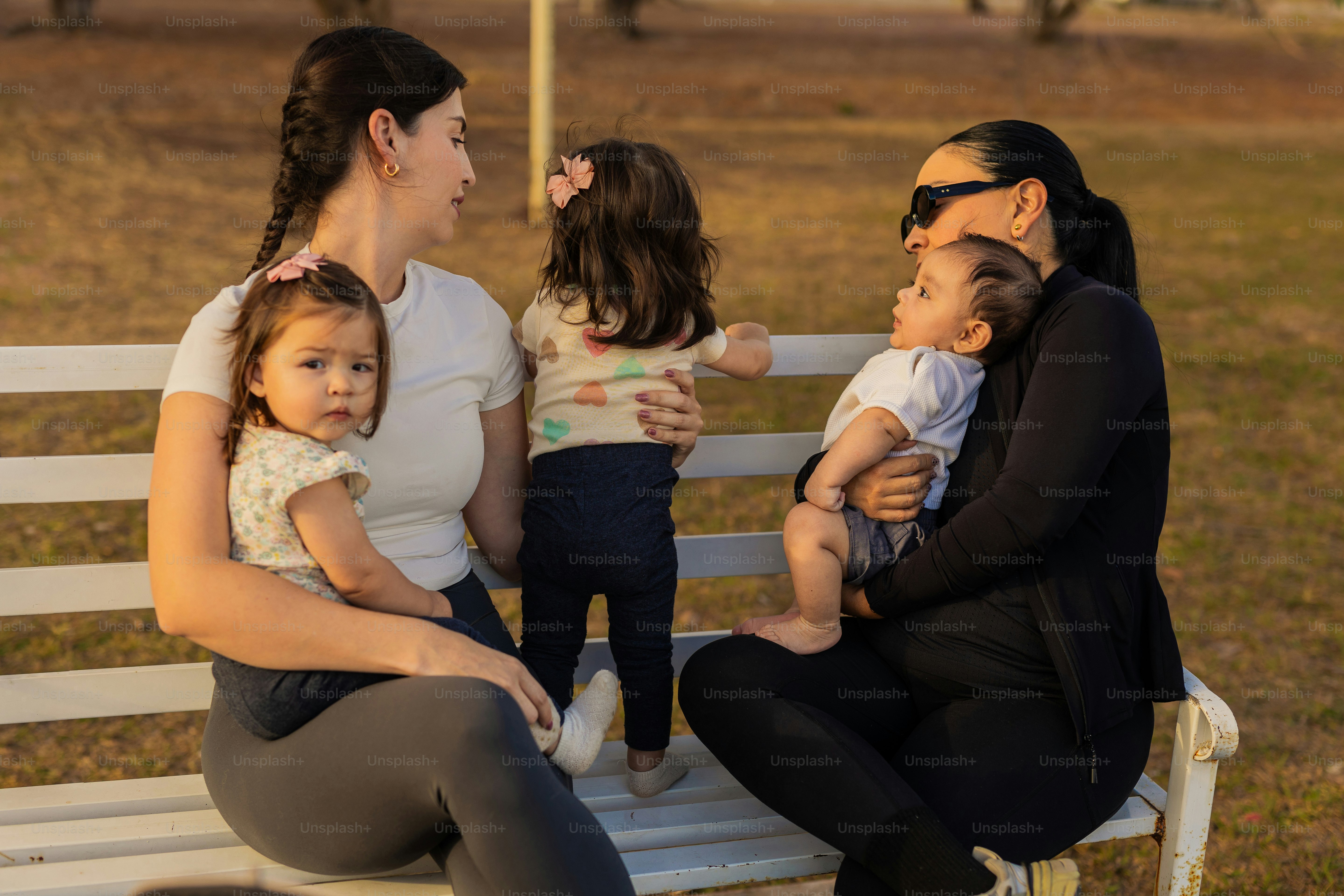 Dua wanita dengan bayi duduk di bangku taman.
