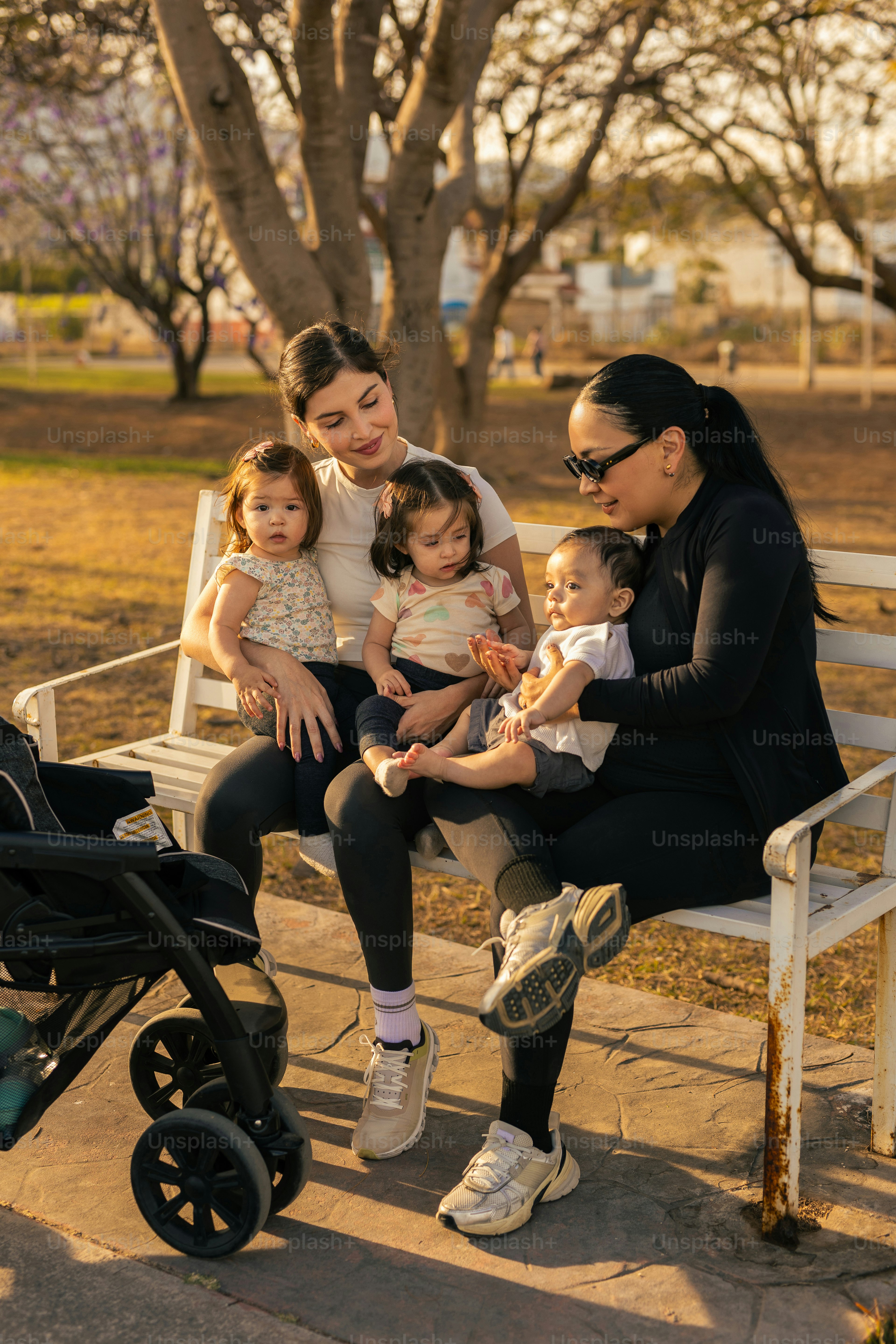 Dua wanita dan tiga bayi duduk di bangku taman.