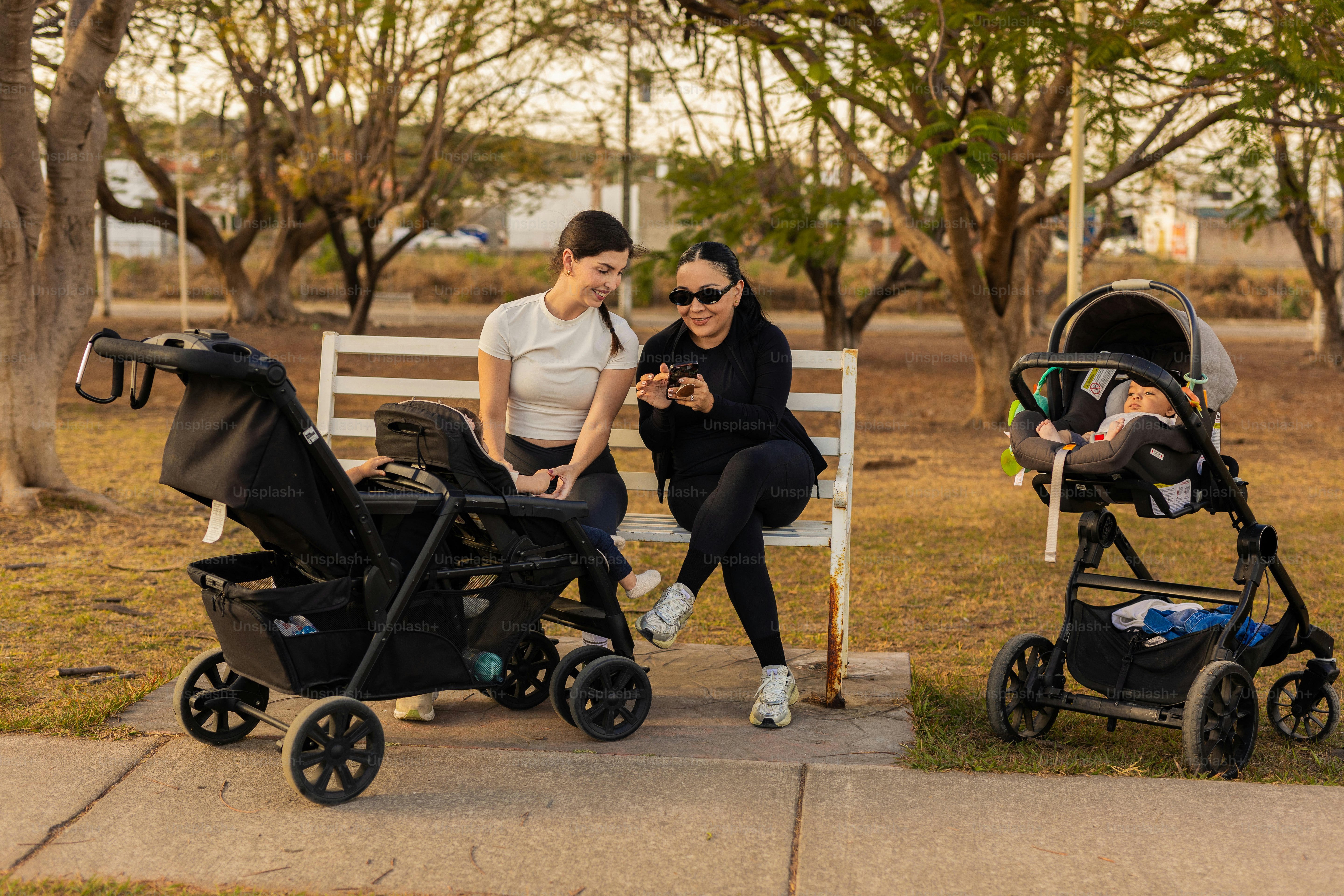Dua wanita duduk di bangku dengan kereta bayi