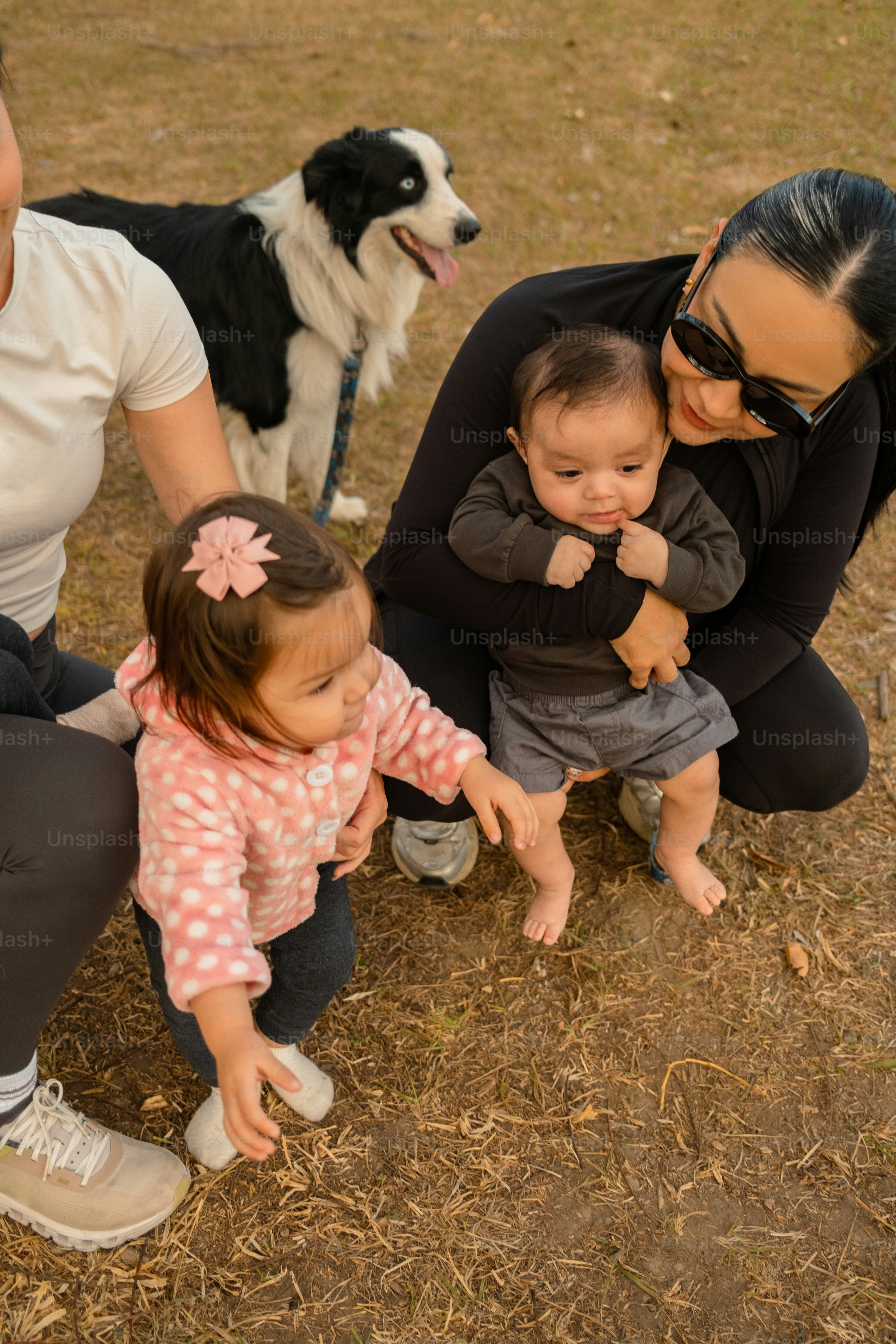 Wanita menggendong bayi dengan balita dan anjing di dekatnya