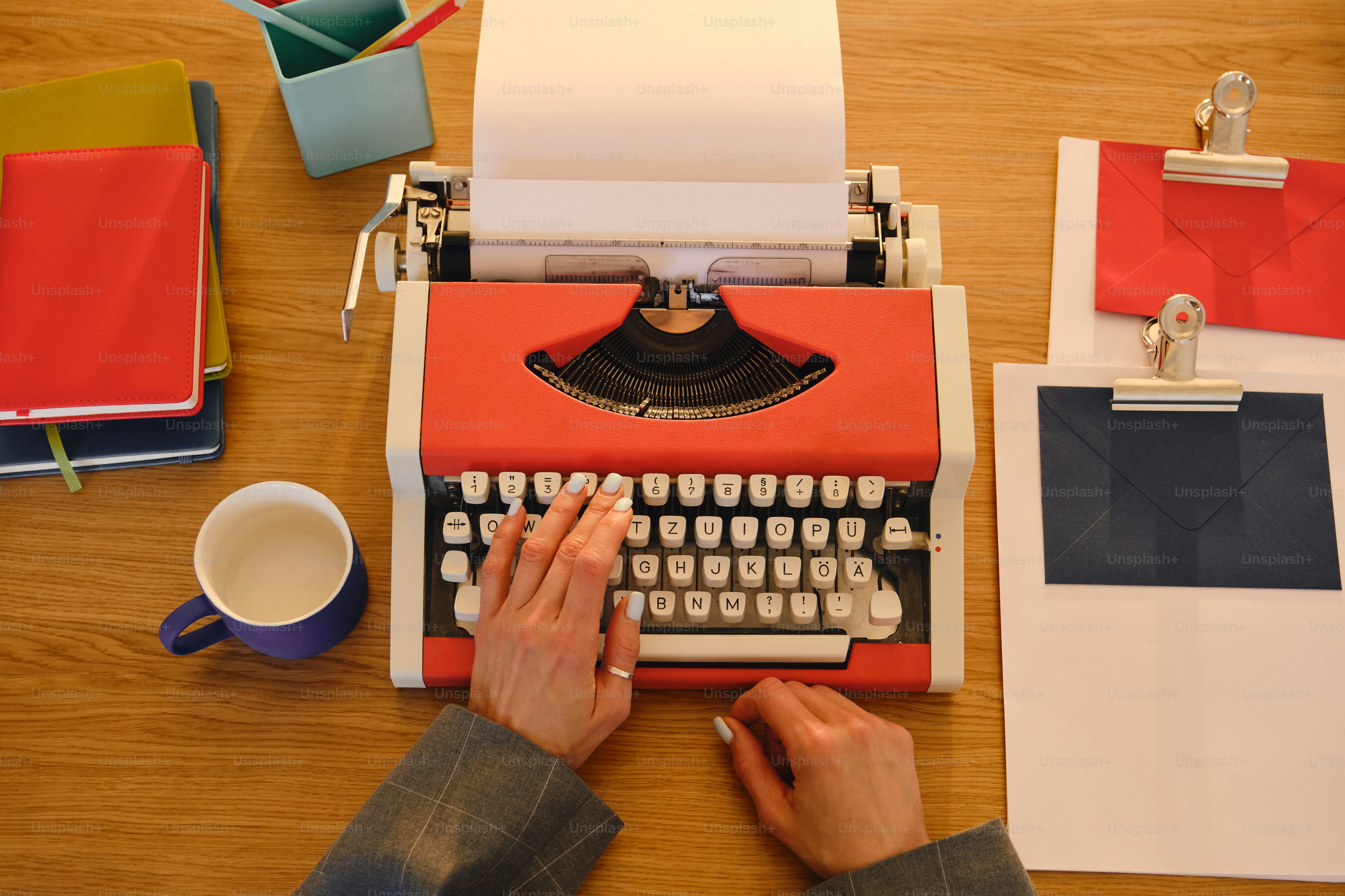 Hands typing on a vintage red typewriter with coffee.