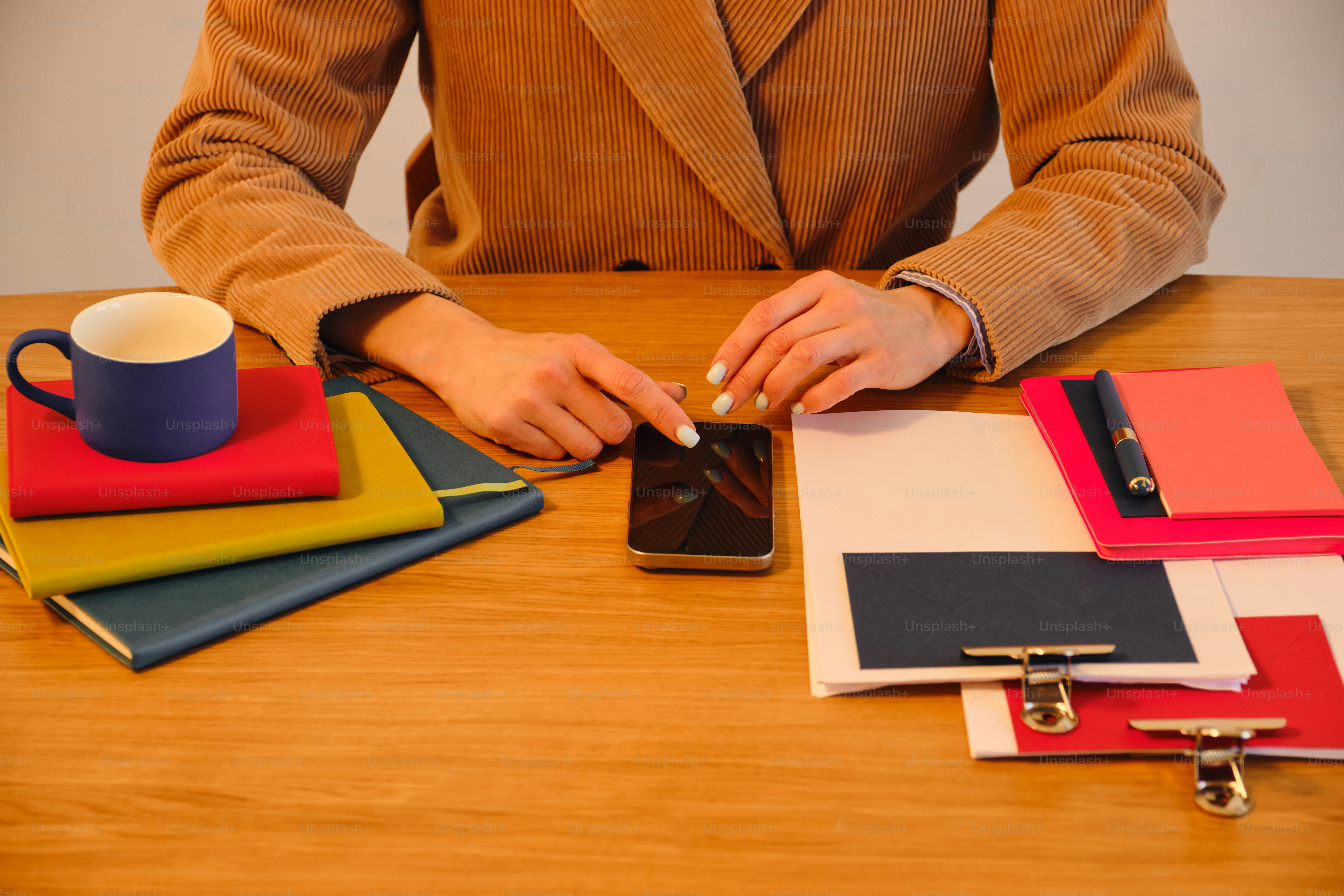 Hands using smartphone on a desk with notebooks.