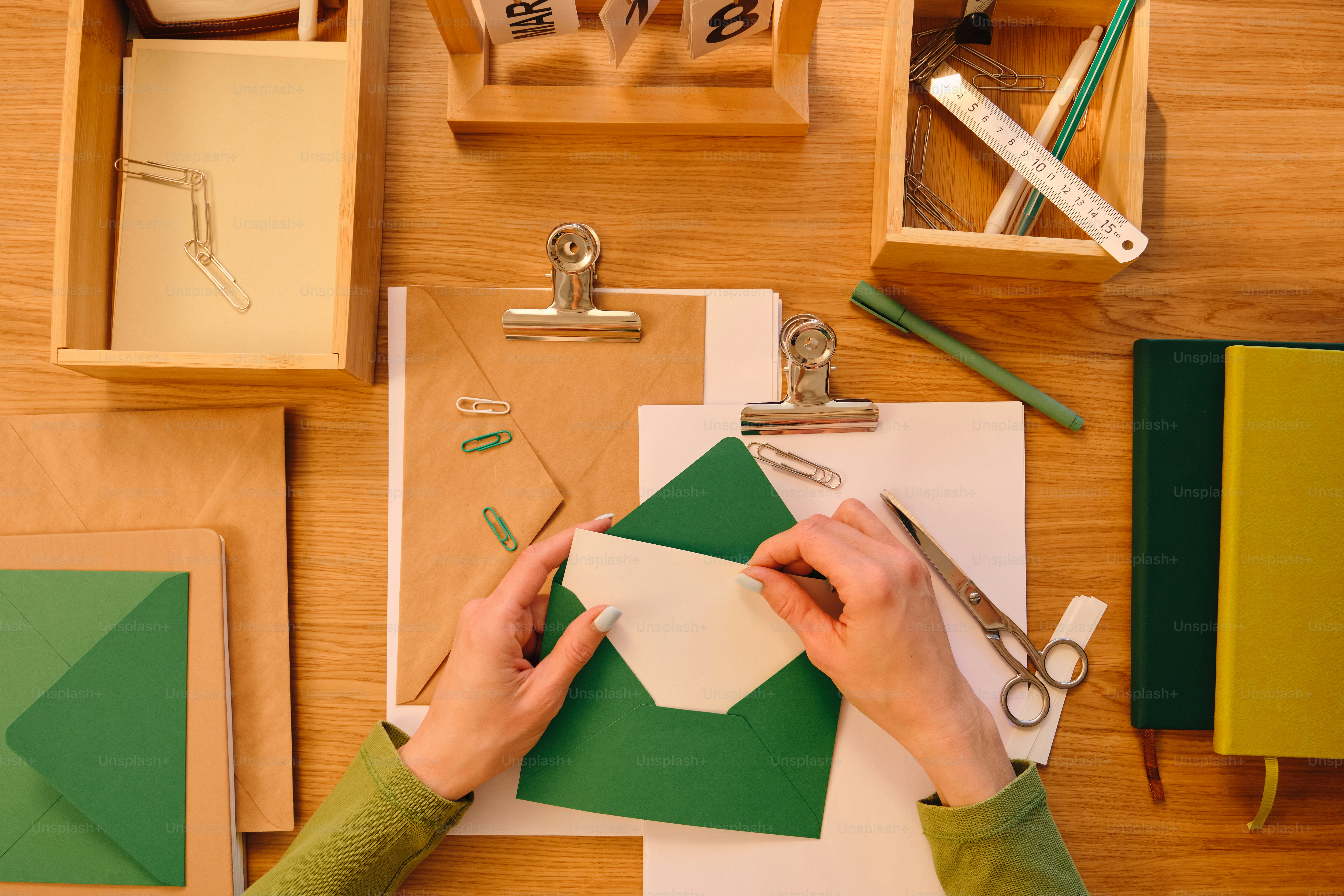 Hands inserting letter into green envelope on wooden desk