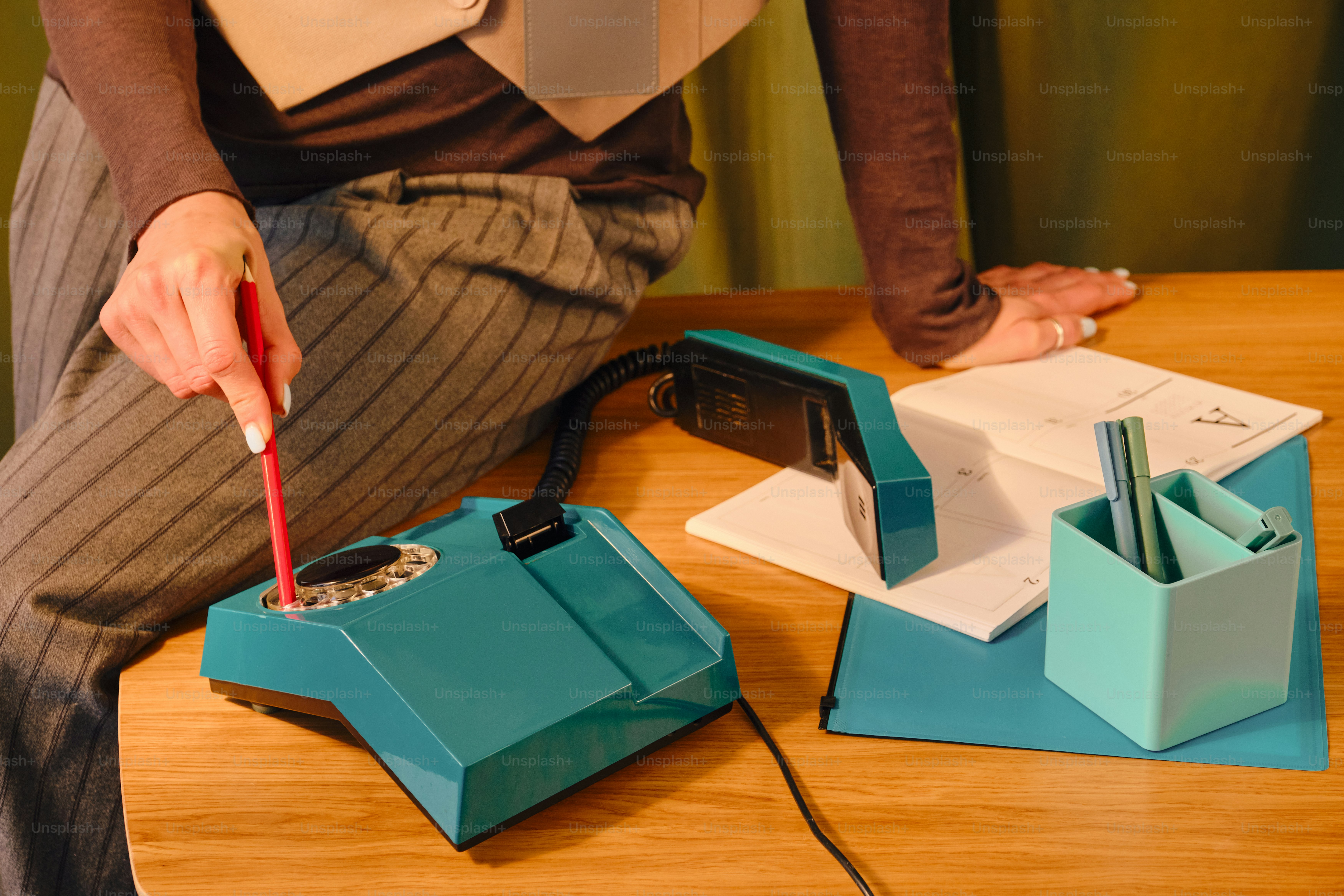 Person using a rotary dial phone on a wooden desk.