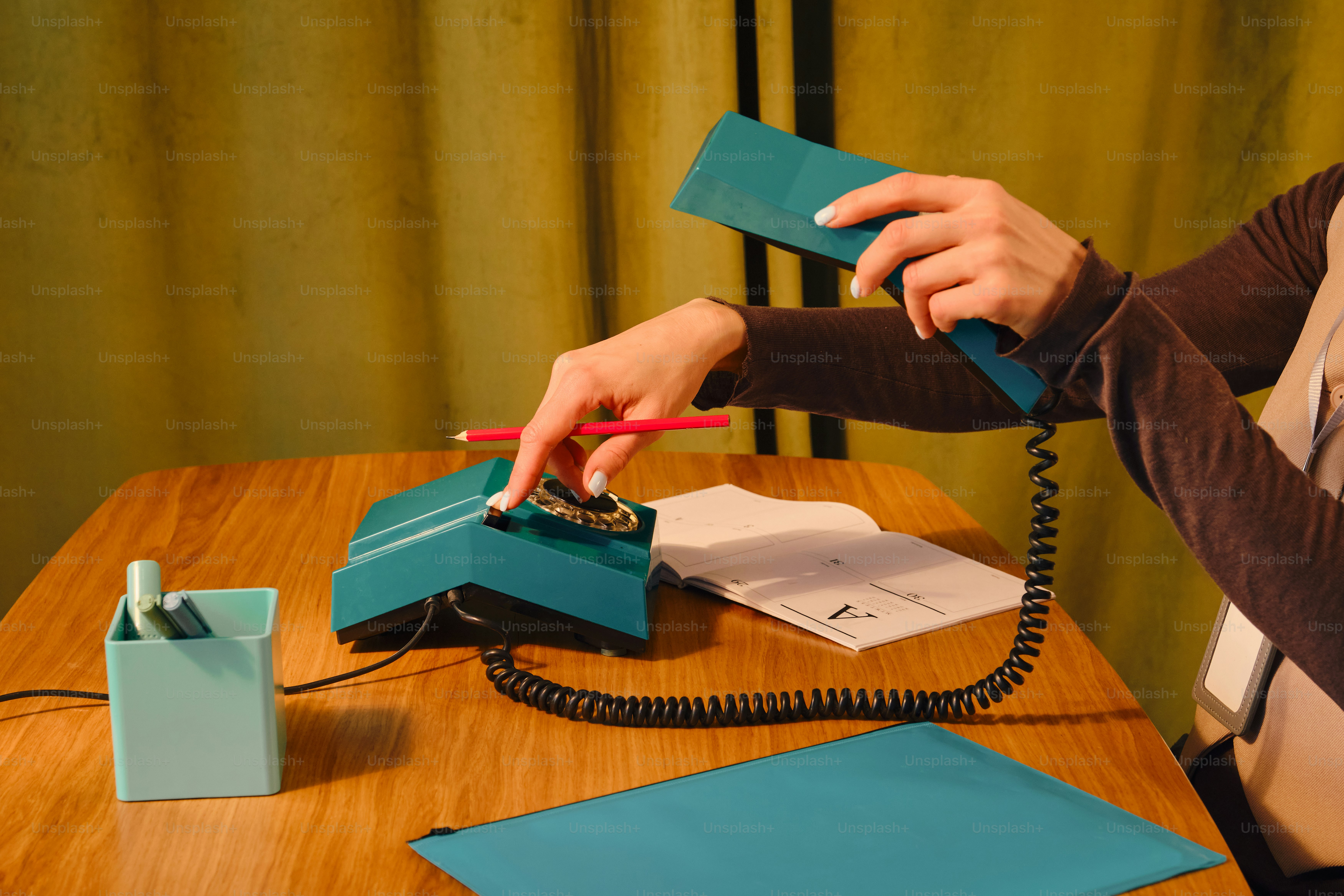 Hands dialing a teal rotary phone with a pencil.
