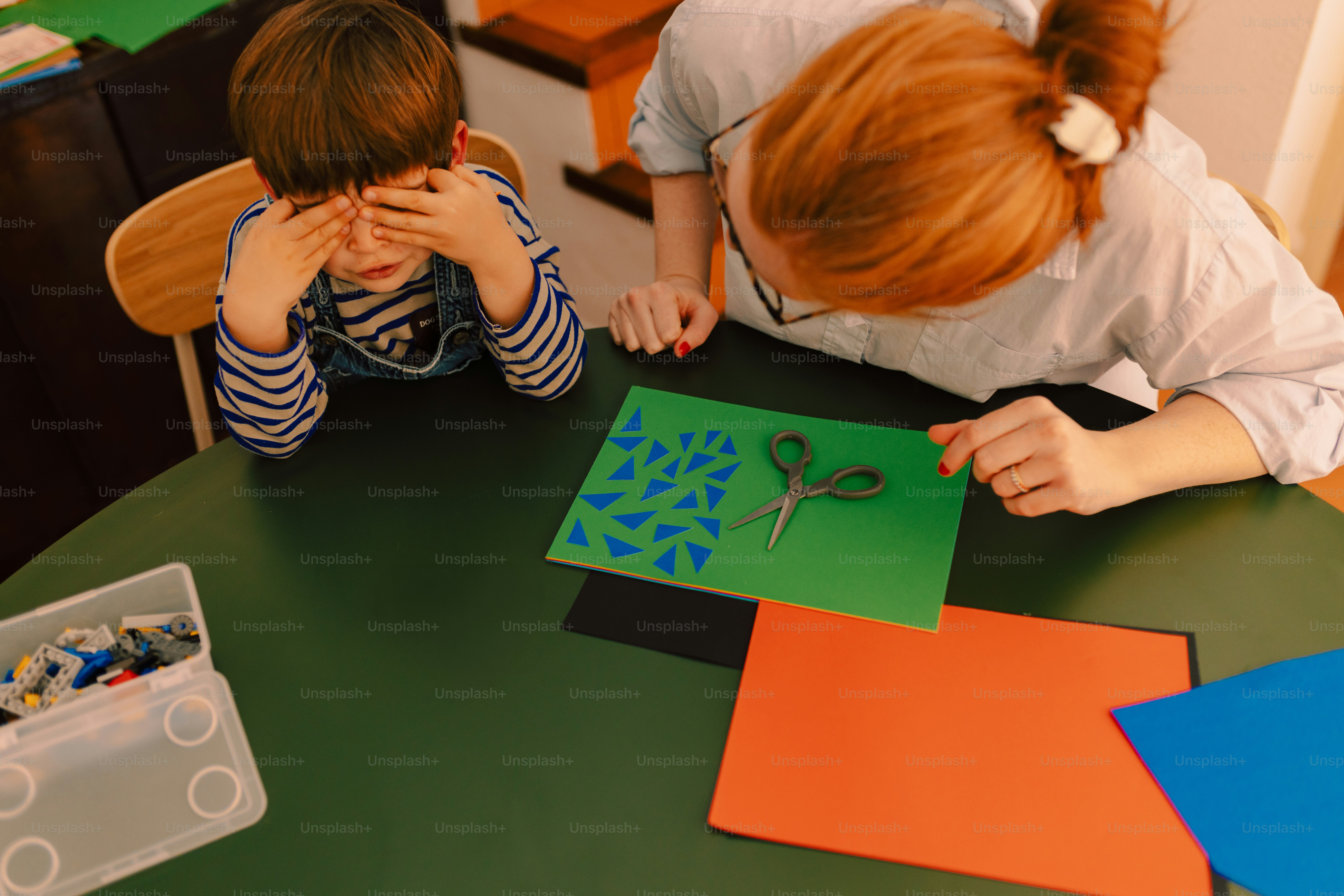 Woman teaching child crafting with scissors and paper.