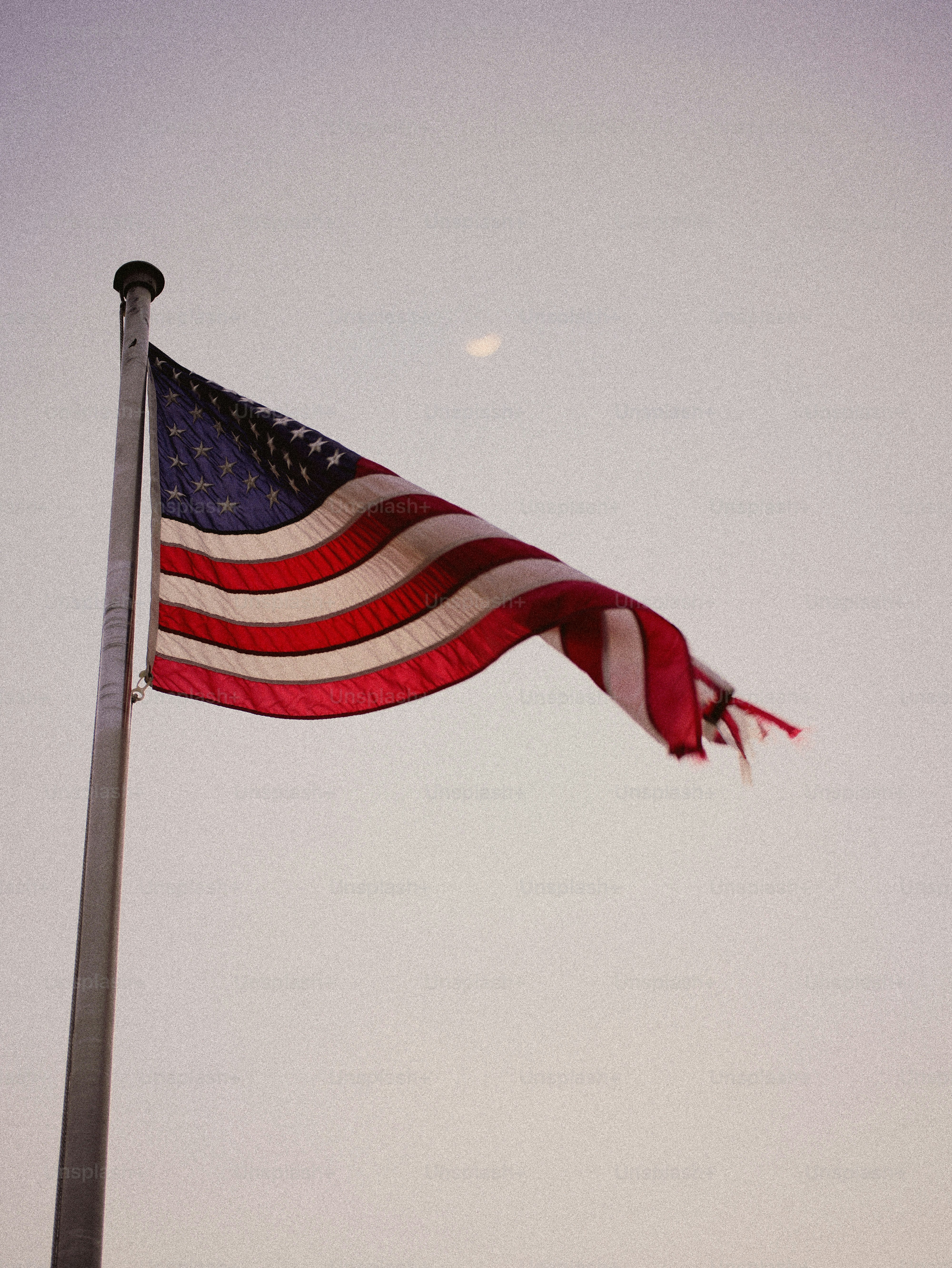 American flag waving on a flagpole against a pale sky