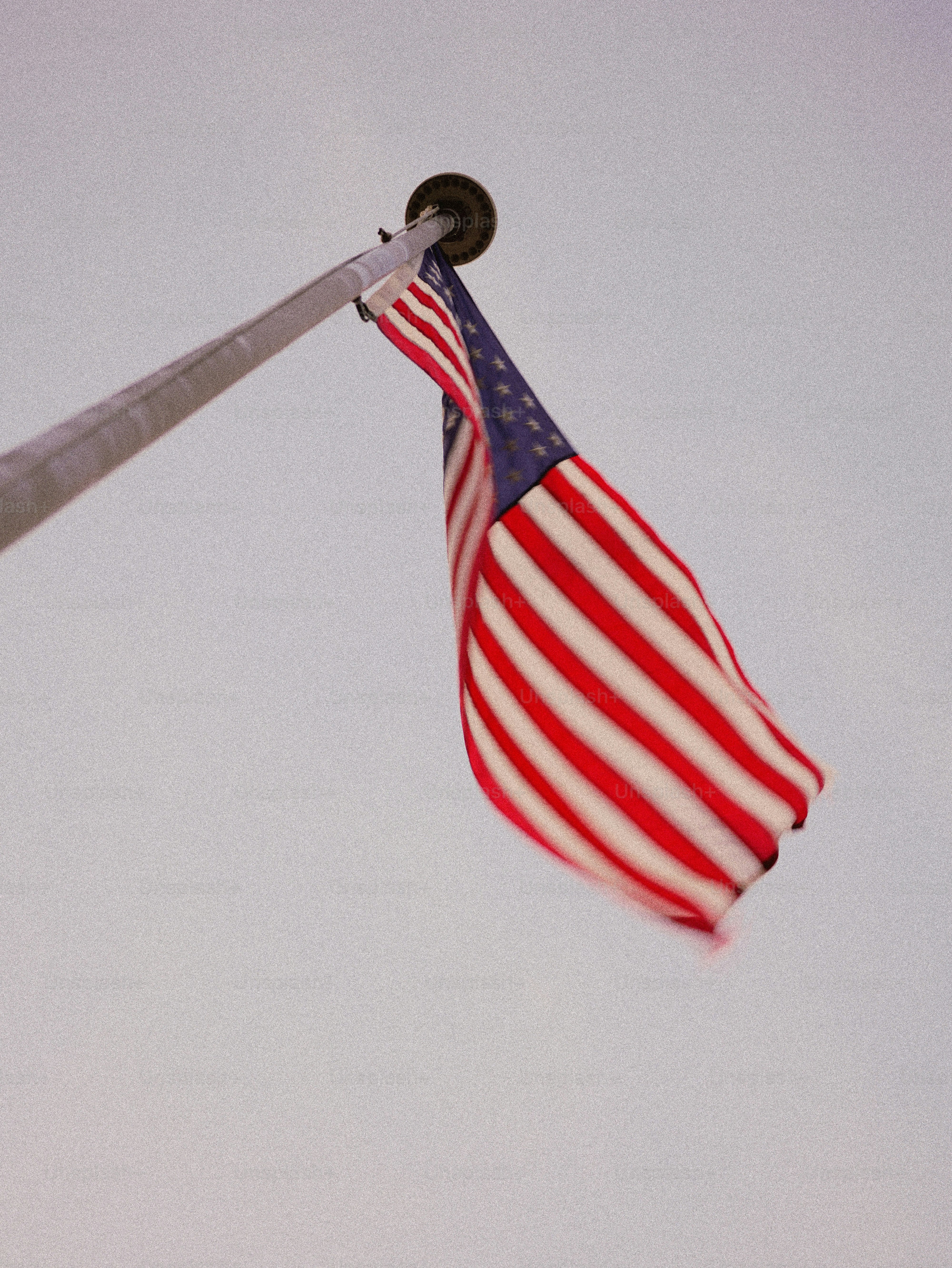 American flag waving on a flagpole against a pale sky.