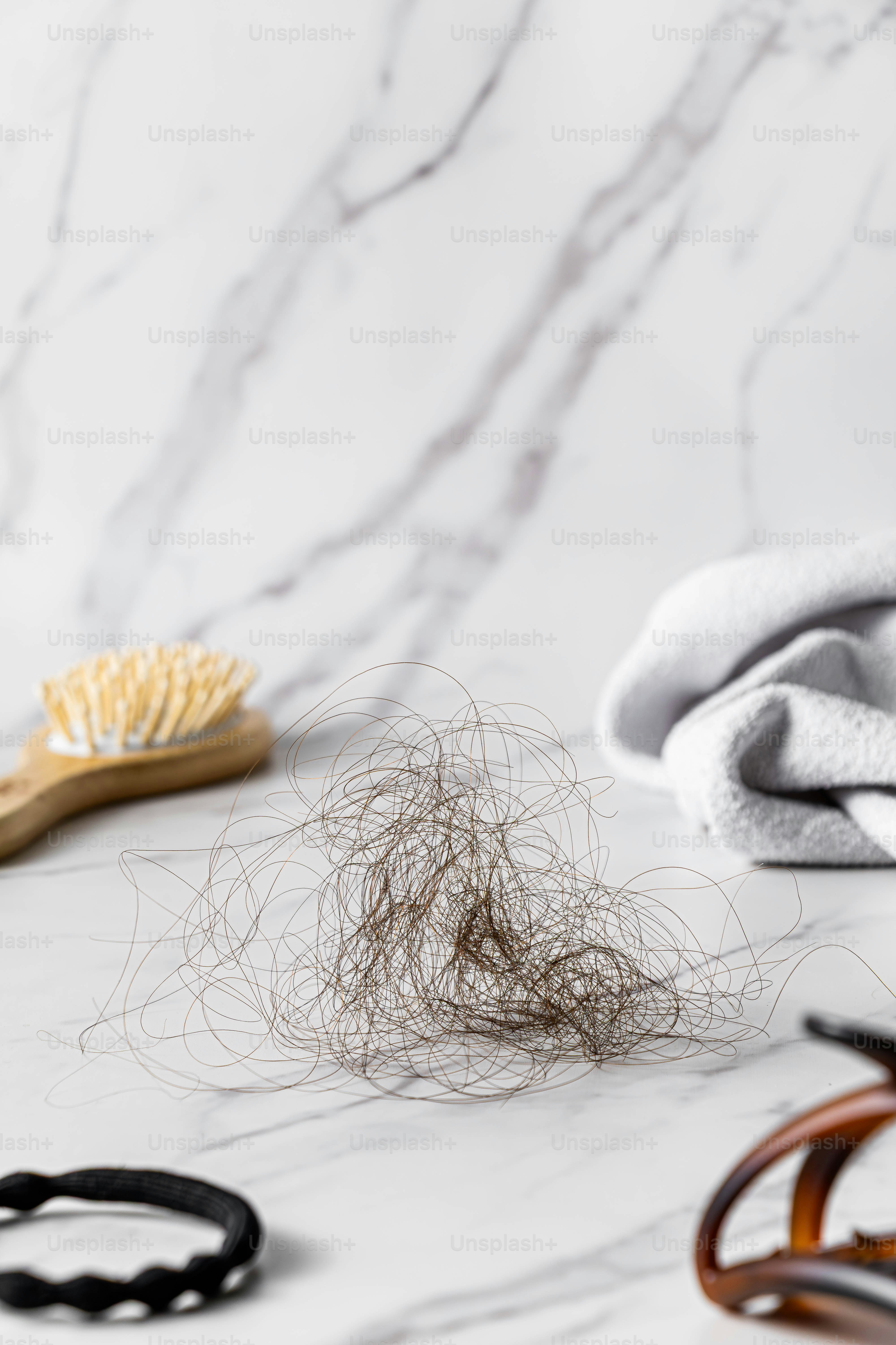 Haufen abgefallener Haare auf Marmor mit Bürste und Klammer