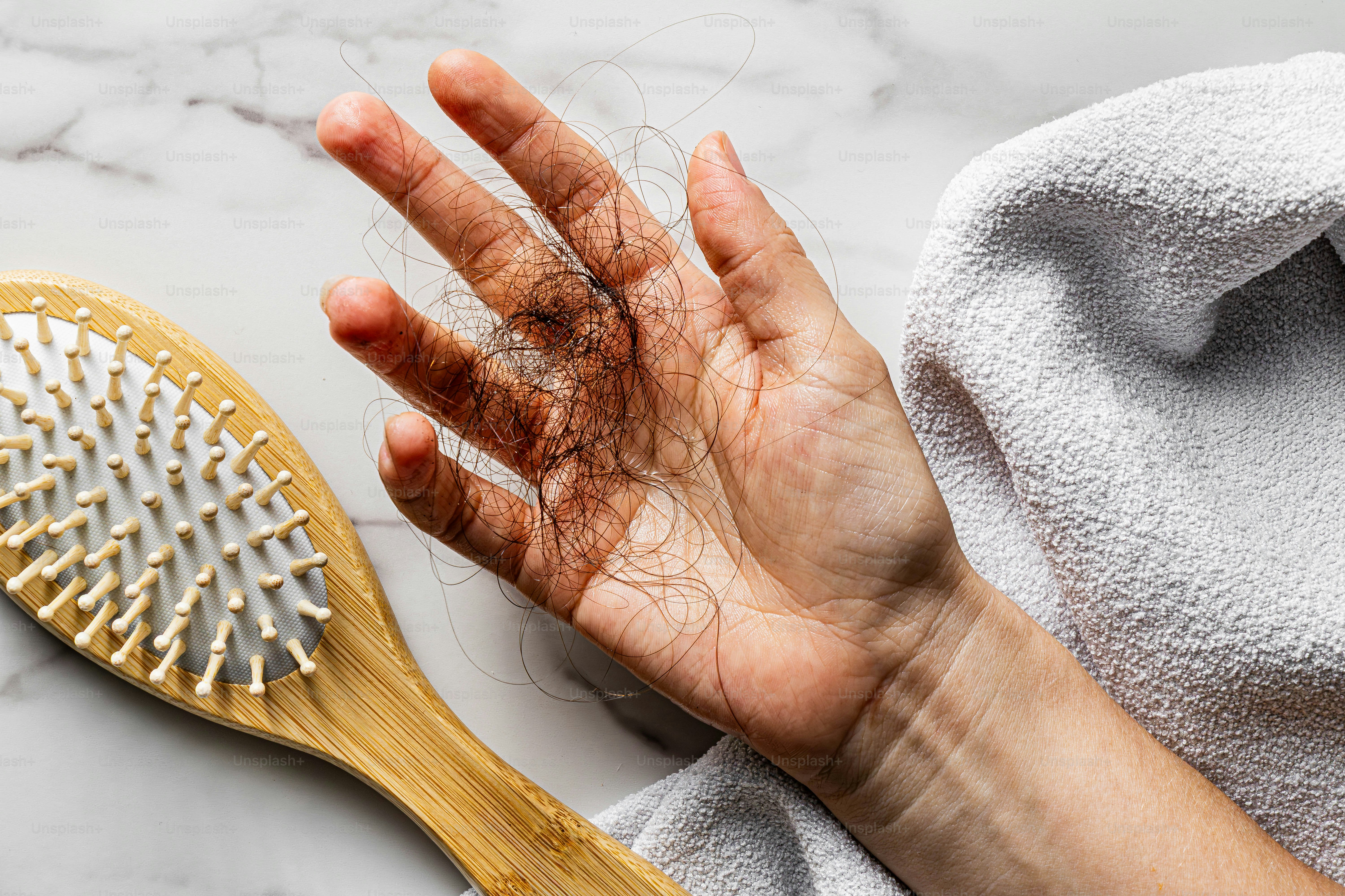 Hand mit heruntergefallenem Haar neben einer Bürste und einem Handtuch