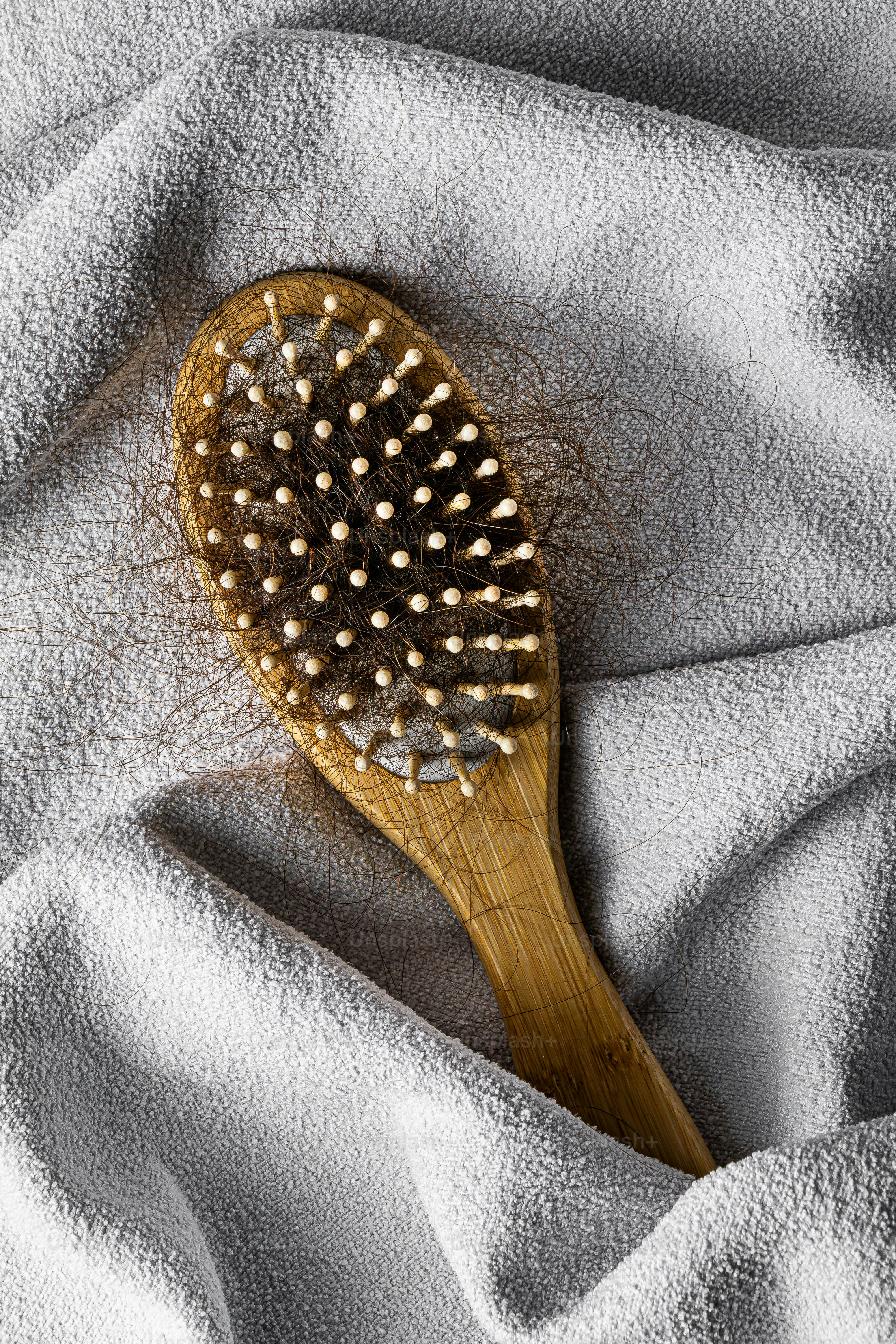 Eine hölzerne Haarbürste mit Haaren auf einem grauen Handtuch