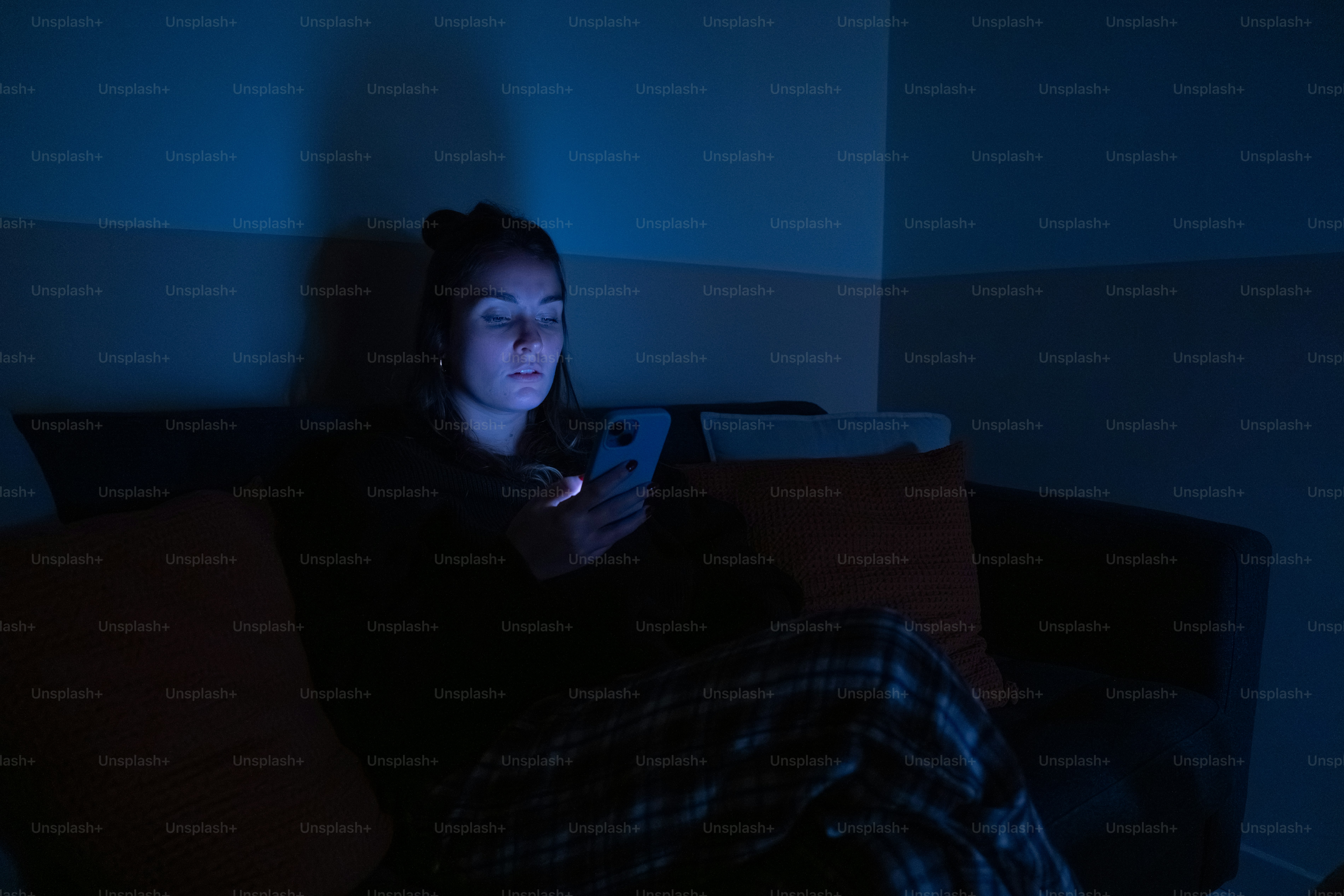Woman illuminated by phone screen on couch at night