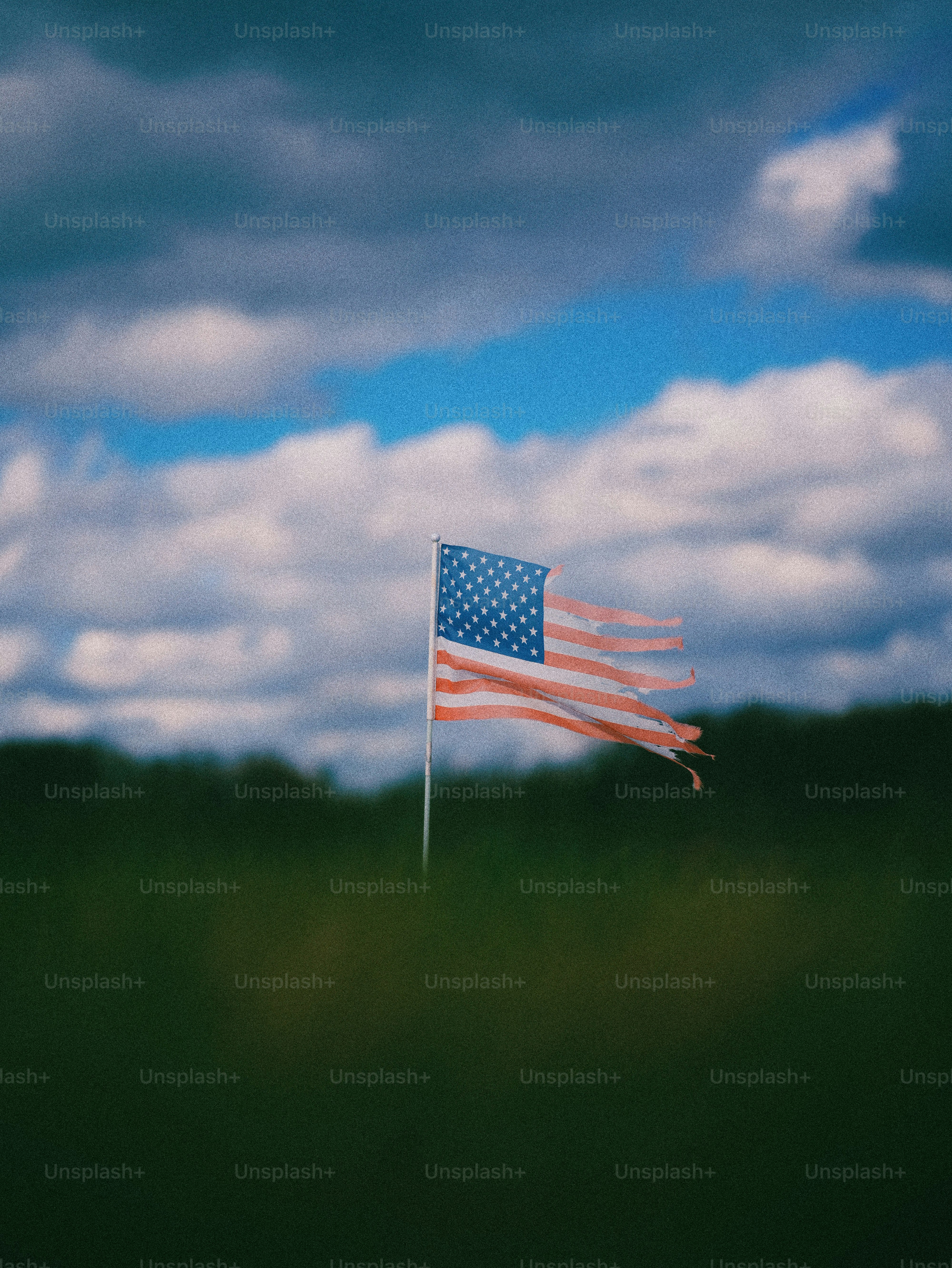 Tattered american flag waves against a cloudy sky