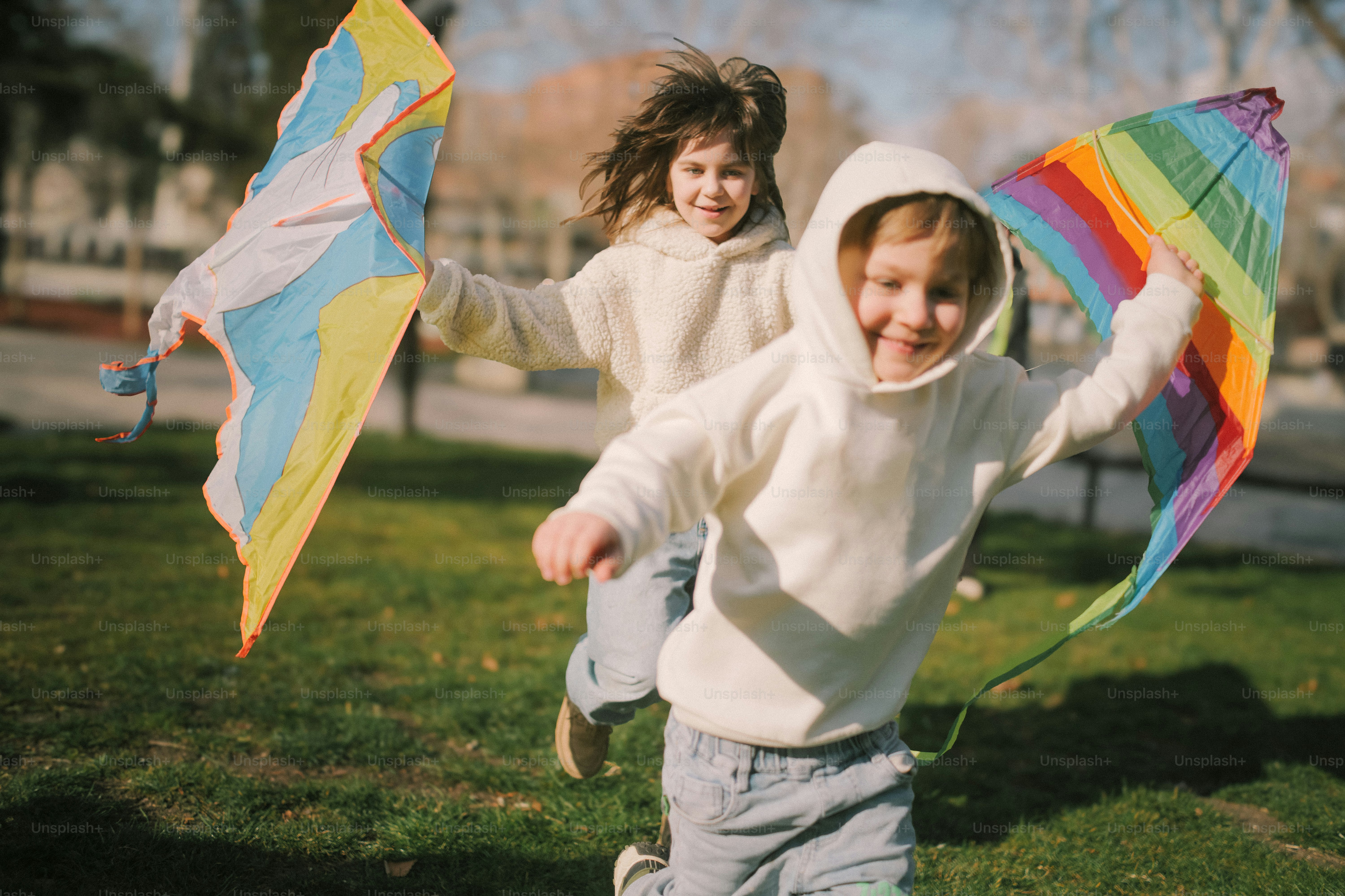 Two children running with colorful kites in a park