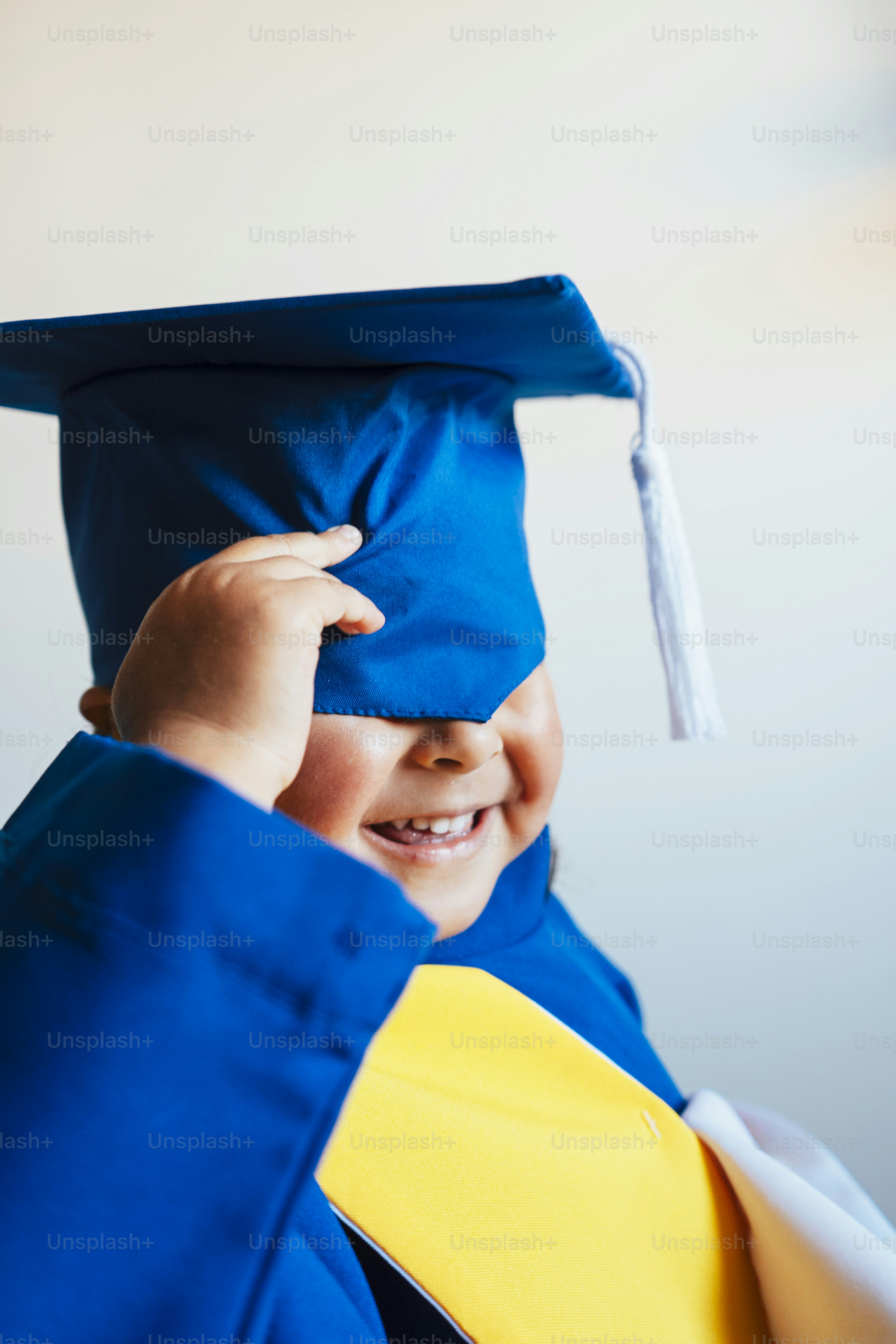 A child in a blue graduation cap and gown smiles. photo – Education ...