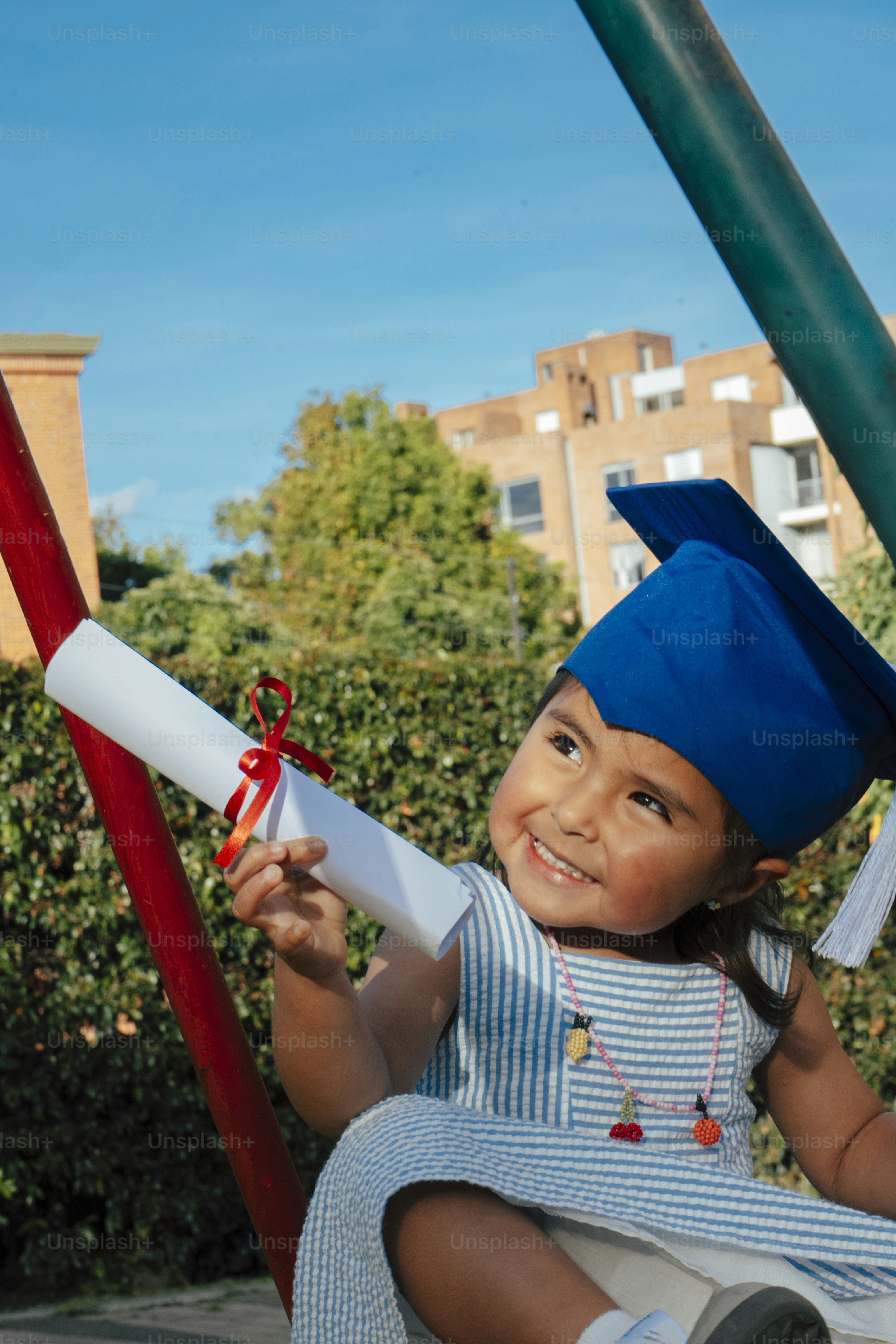 A smiling child in a graduation cap holds a diploma. photo – Education ...