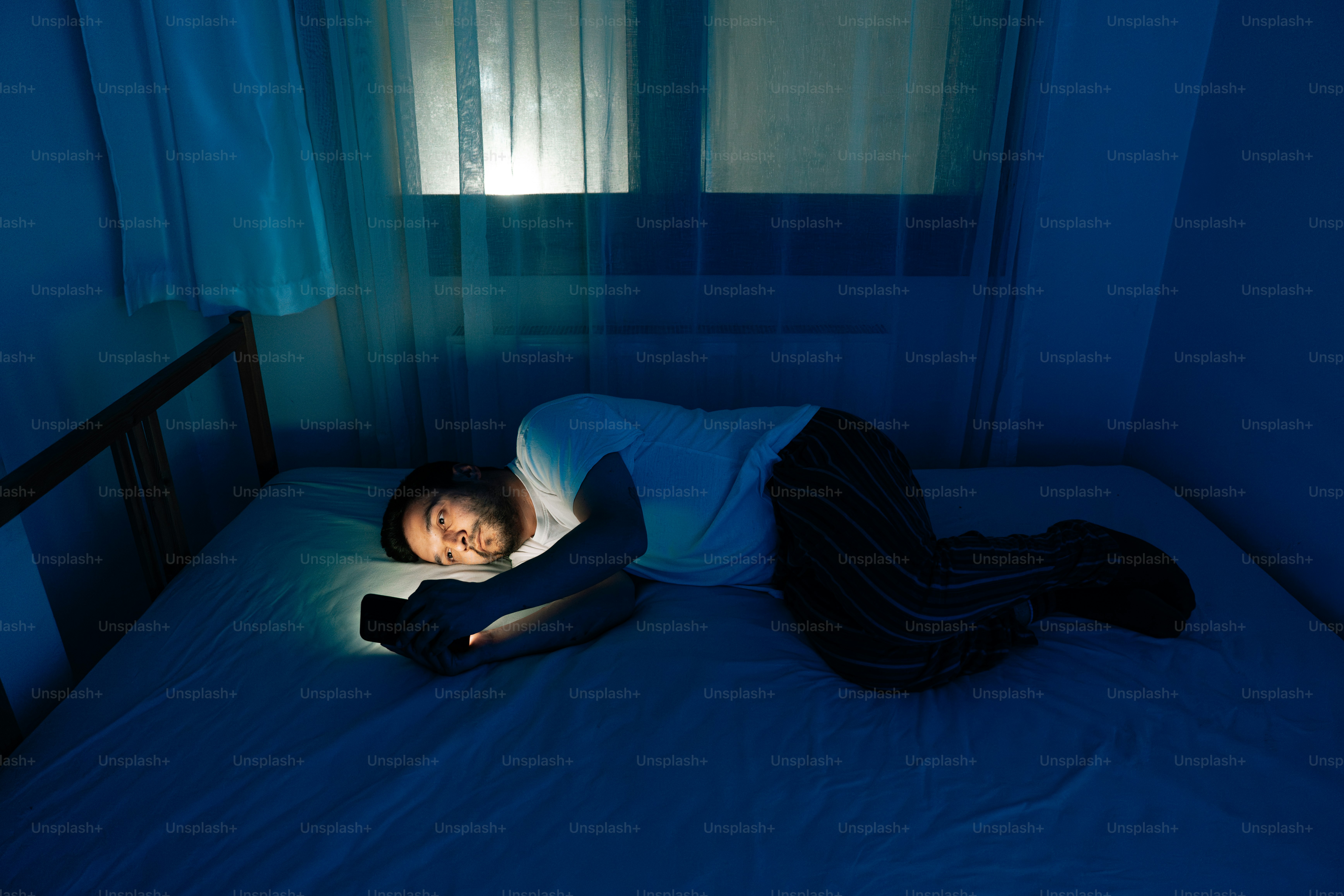 Person scrolling on a phone in bed in a dark room late at night