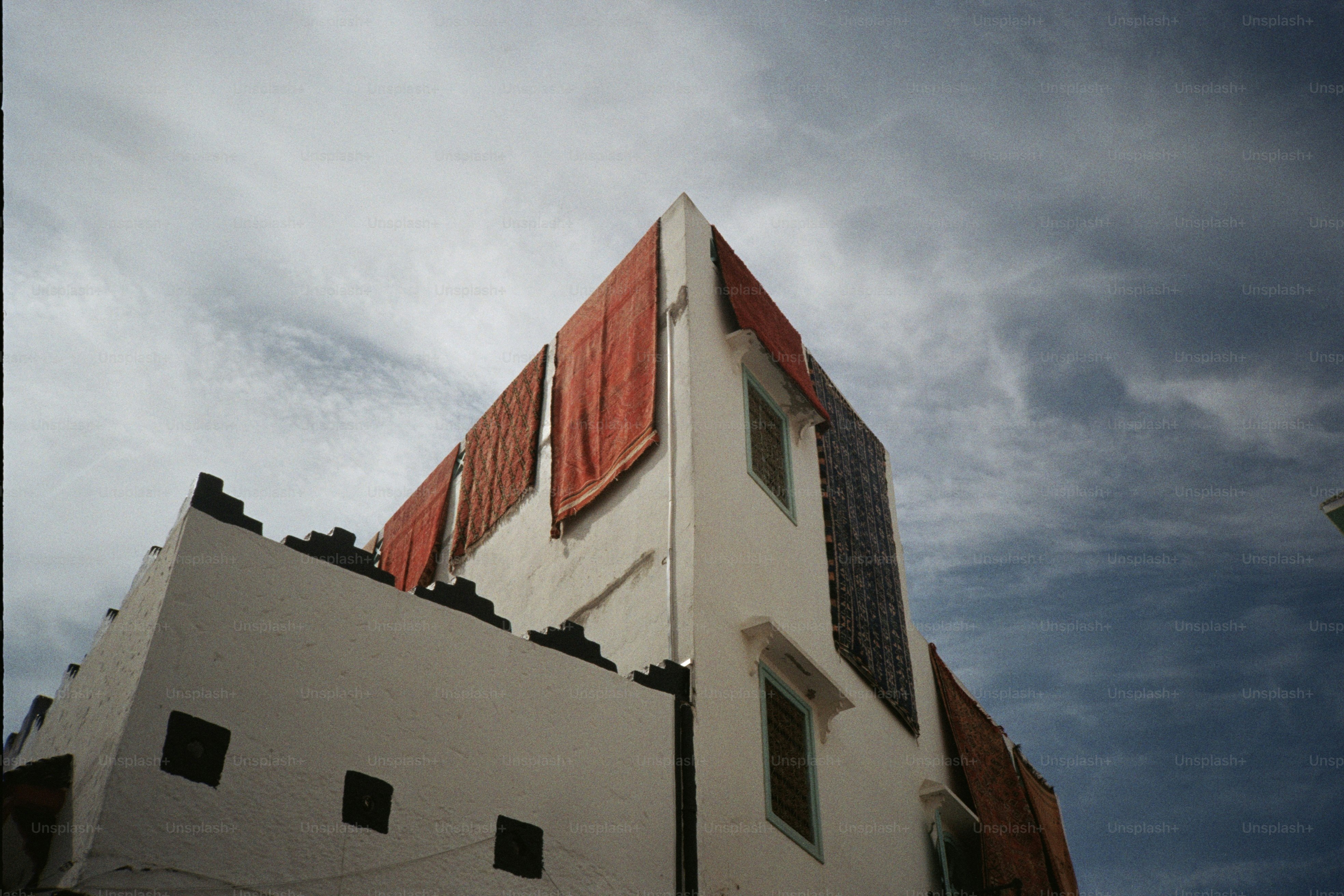 Textiles hang drying on a white building exterior. photo – Architecture ...