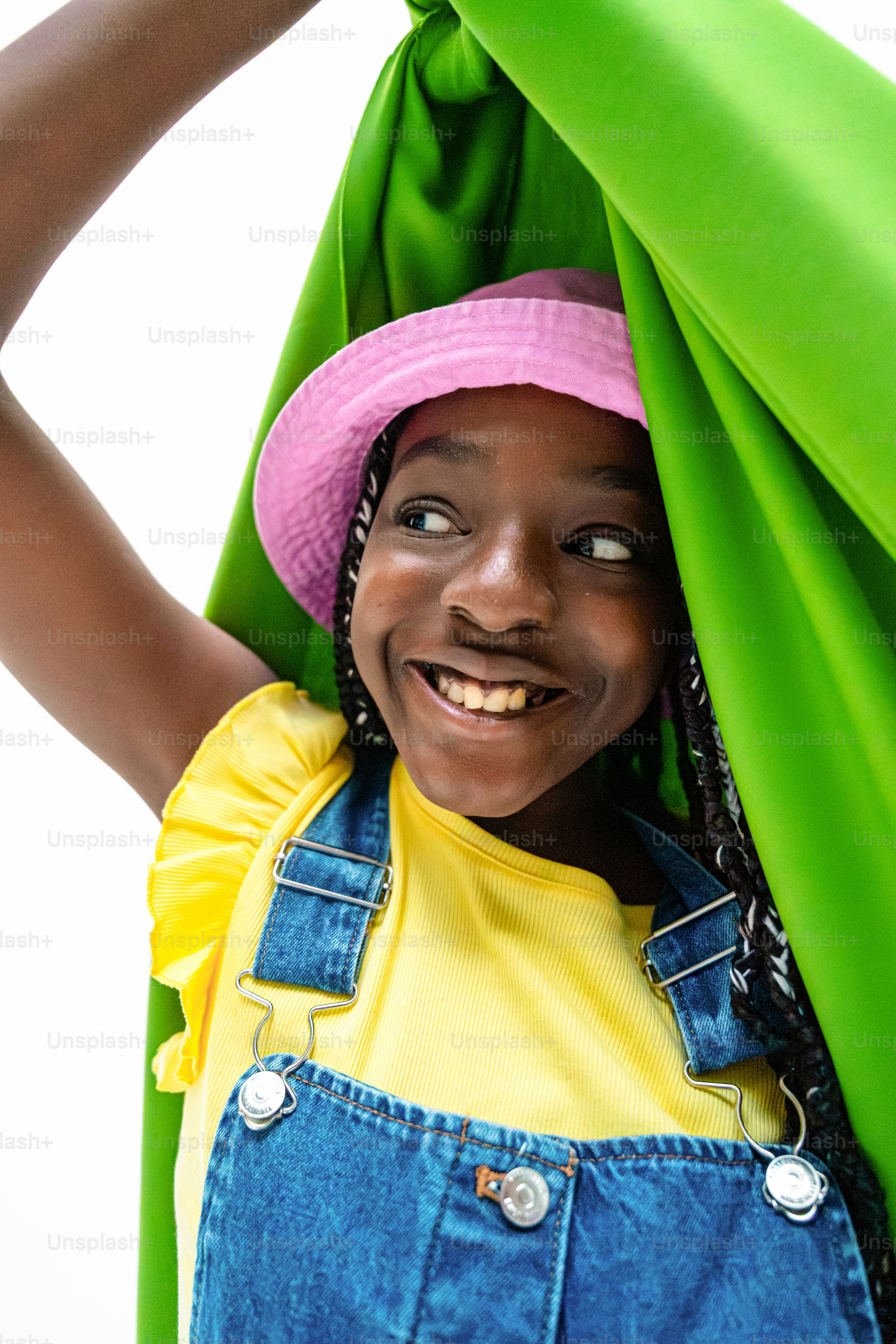 Una chica negra sonriente con sombrero rosa y peto.